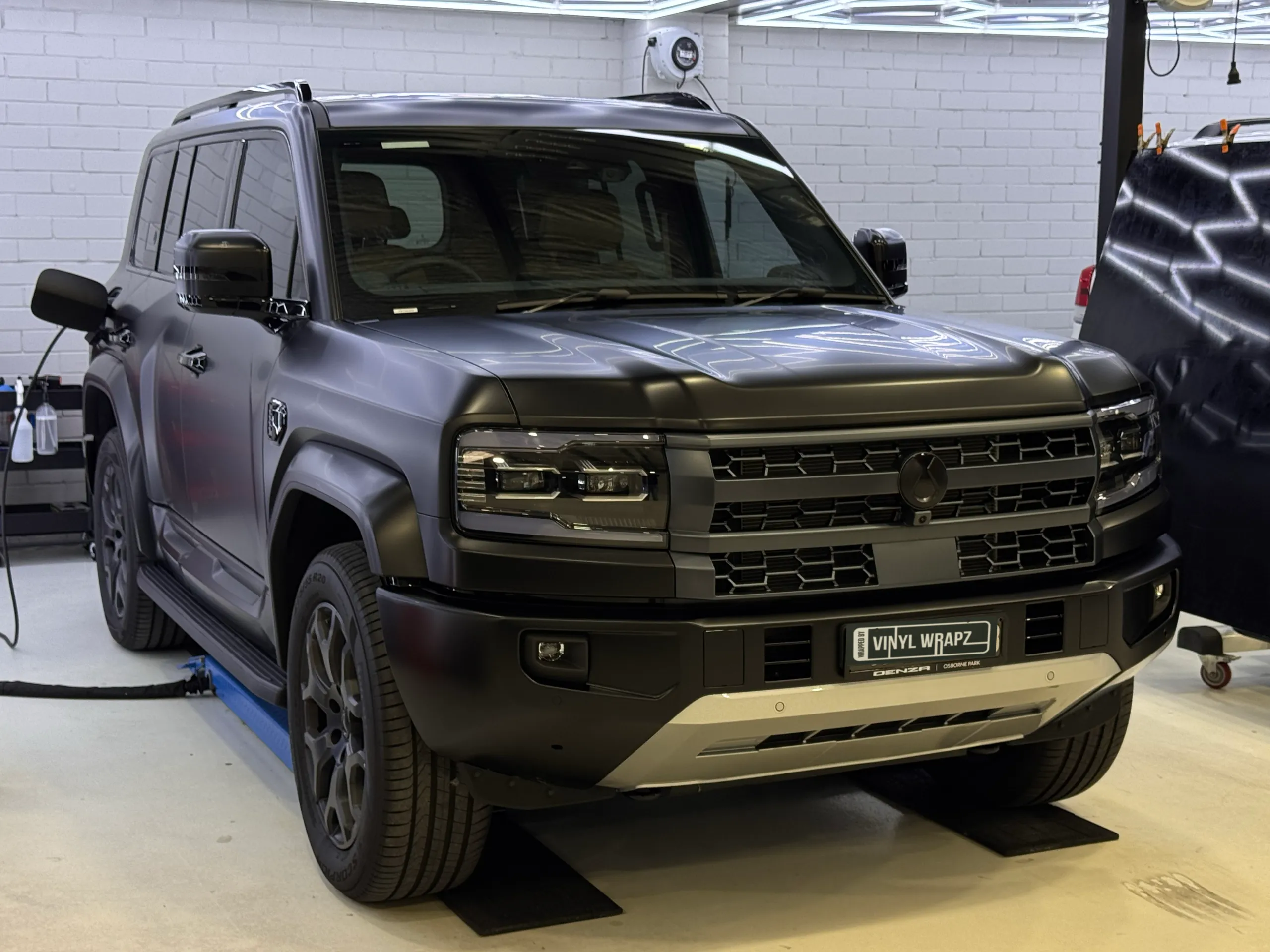Satin grey Denza B5 viewed from the front quarter on a workshop lift