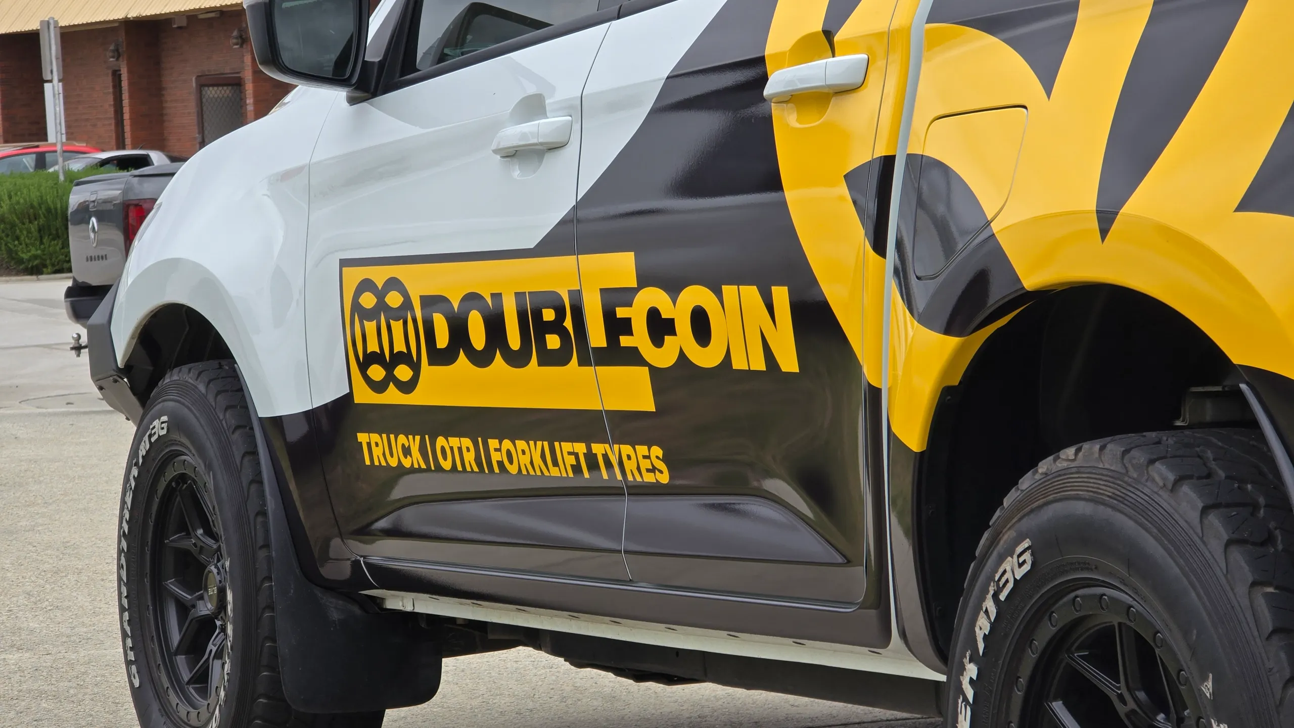 Yellow Double Coin logo across the Mazda BT-50 doors beside black and yellow tray graphics