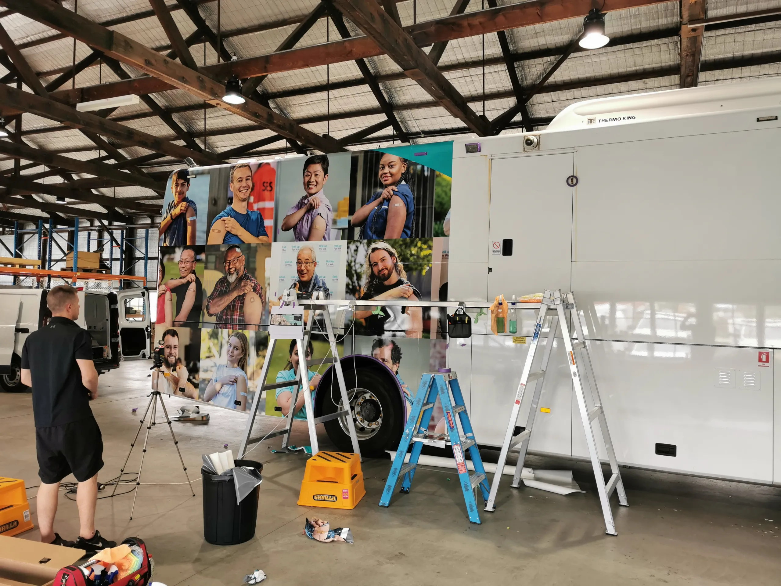 Installers applying coach graphics beside the workshop ladder