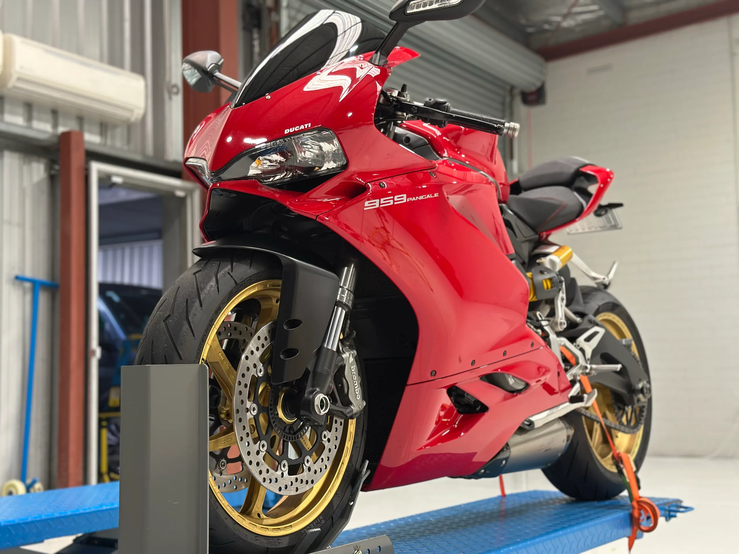 Red Ducati 959 Panigale with gold wheels viewed from a low front-quarter angle on a lift