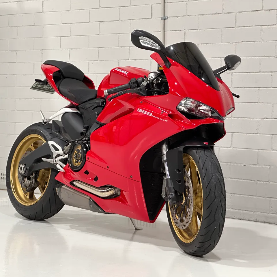 Red Ducati 959 Panigale with gold wheels viewed from the front quarter against a white wall