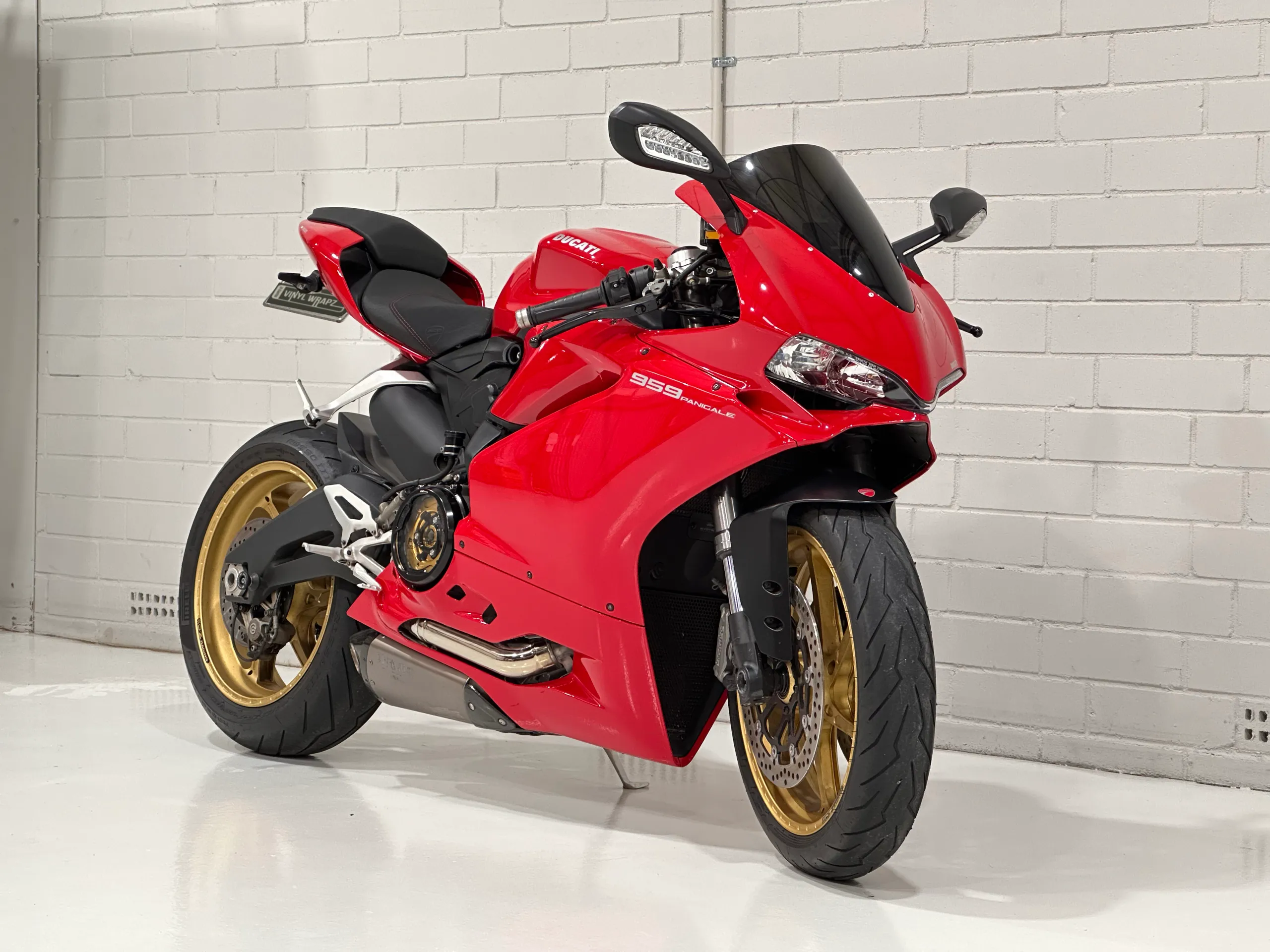 Red Ducati 959 Panigale with gold wheels viewed from the front quarter against a white wall
