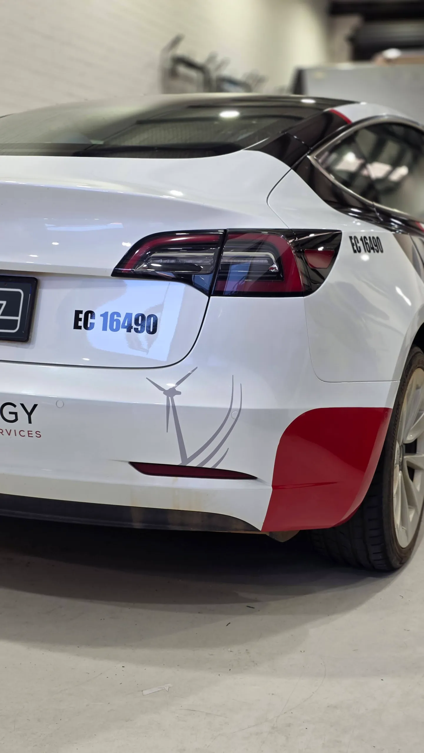 Black and red ESS graphics on the rear corner of a white Tesla Model 3