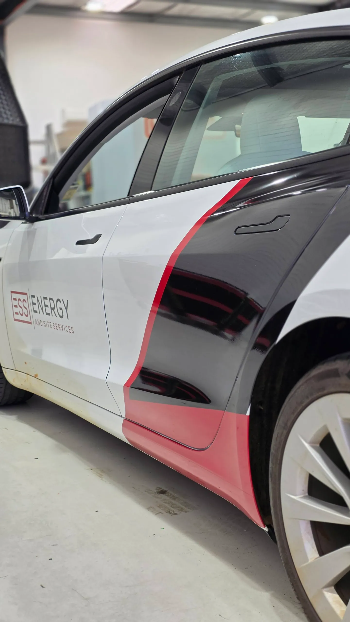 White Tesla Model 3 with black and red ESS Energy and Site Services graphics