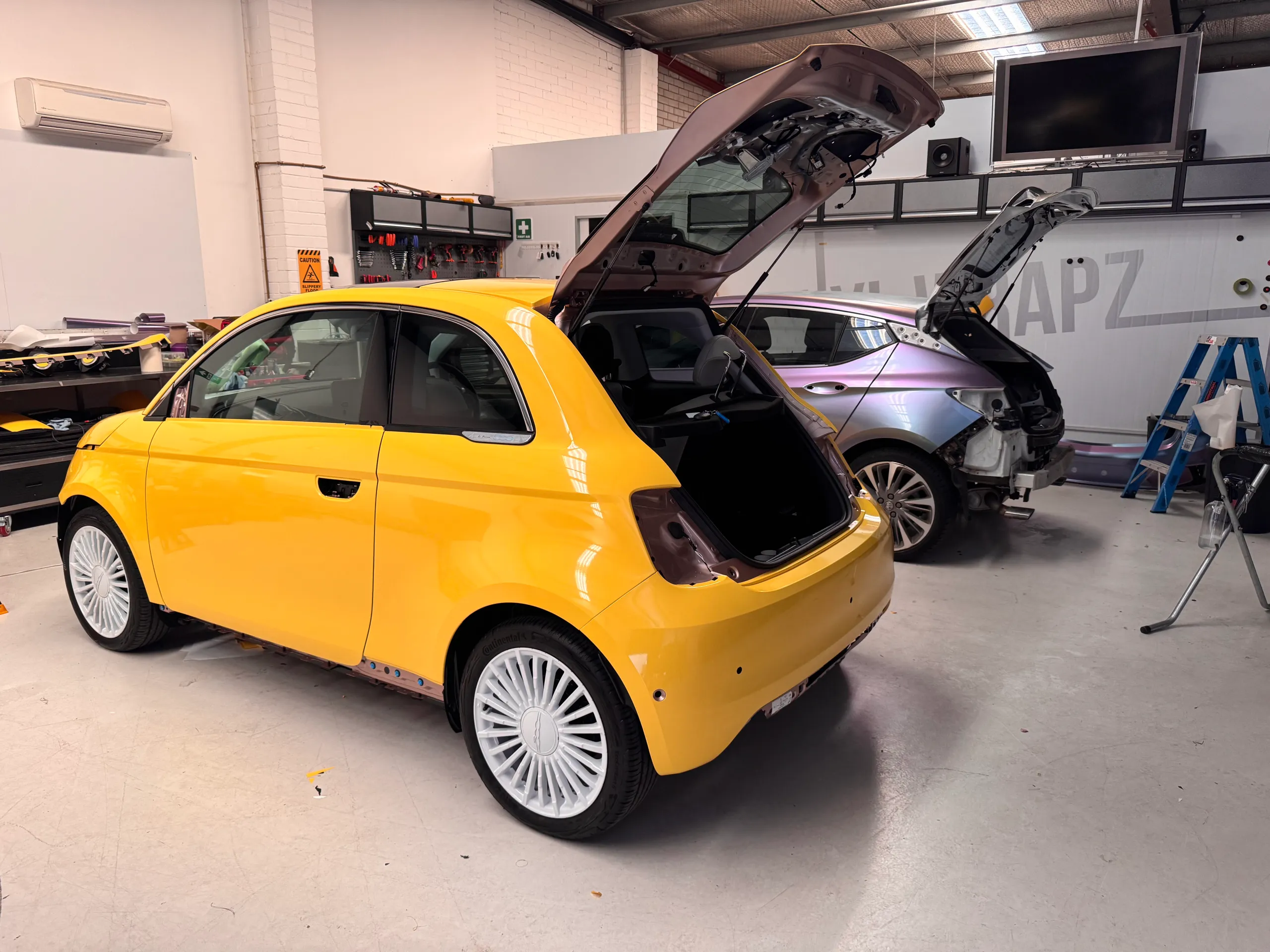 Yellow Fiat 500 with its tailgate open and rear lights removed during workshop preparation