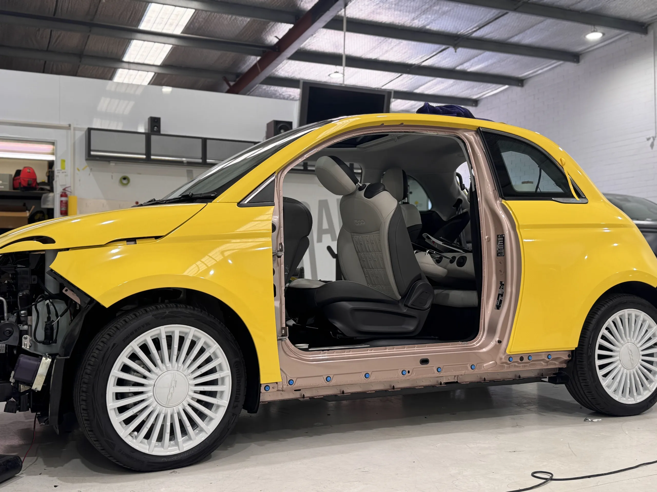 Fiat 500 with its door and front bumper removed, exposing the door opening beside yellow exterior panels