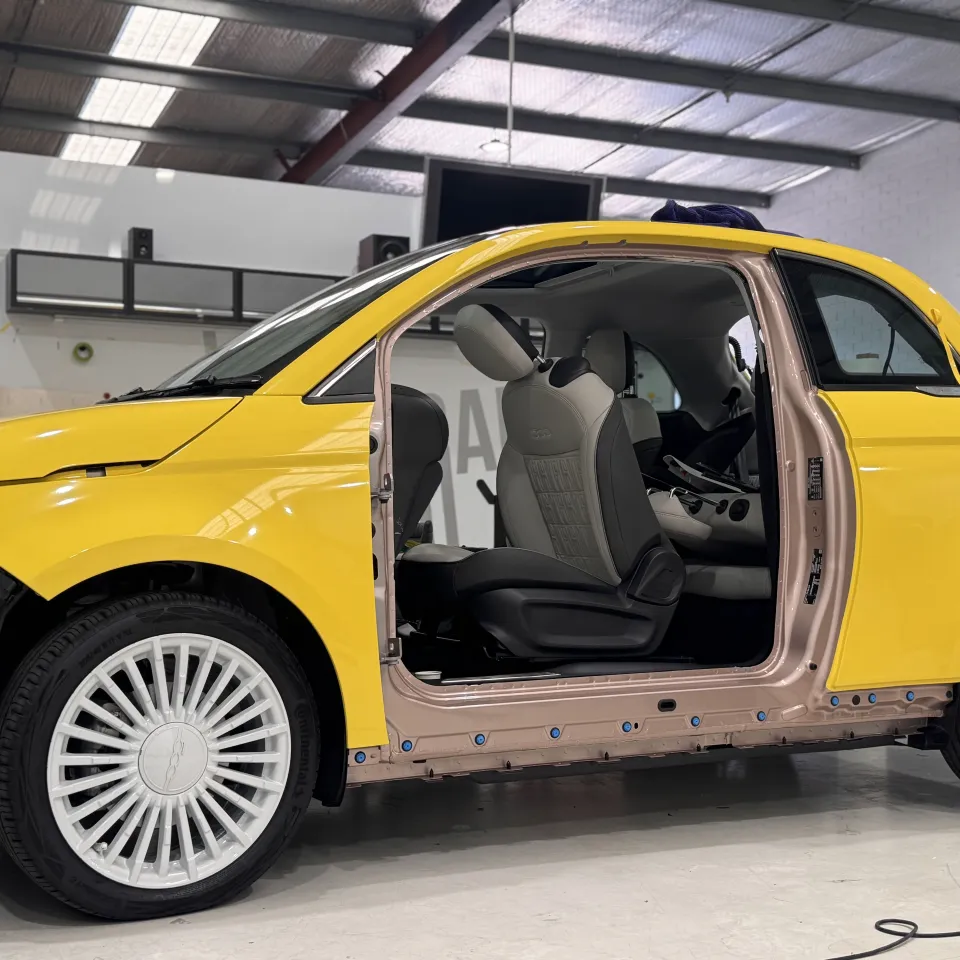 Fiat 500 with its door and front bumper removed, exposing the door opening beside yellow exterior panels