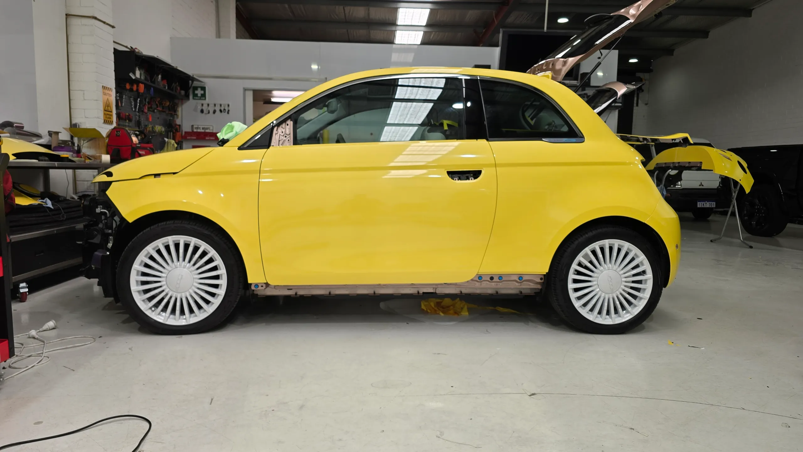 Yellow Fiat 500e during wrapping with bumper and side trim removed