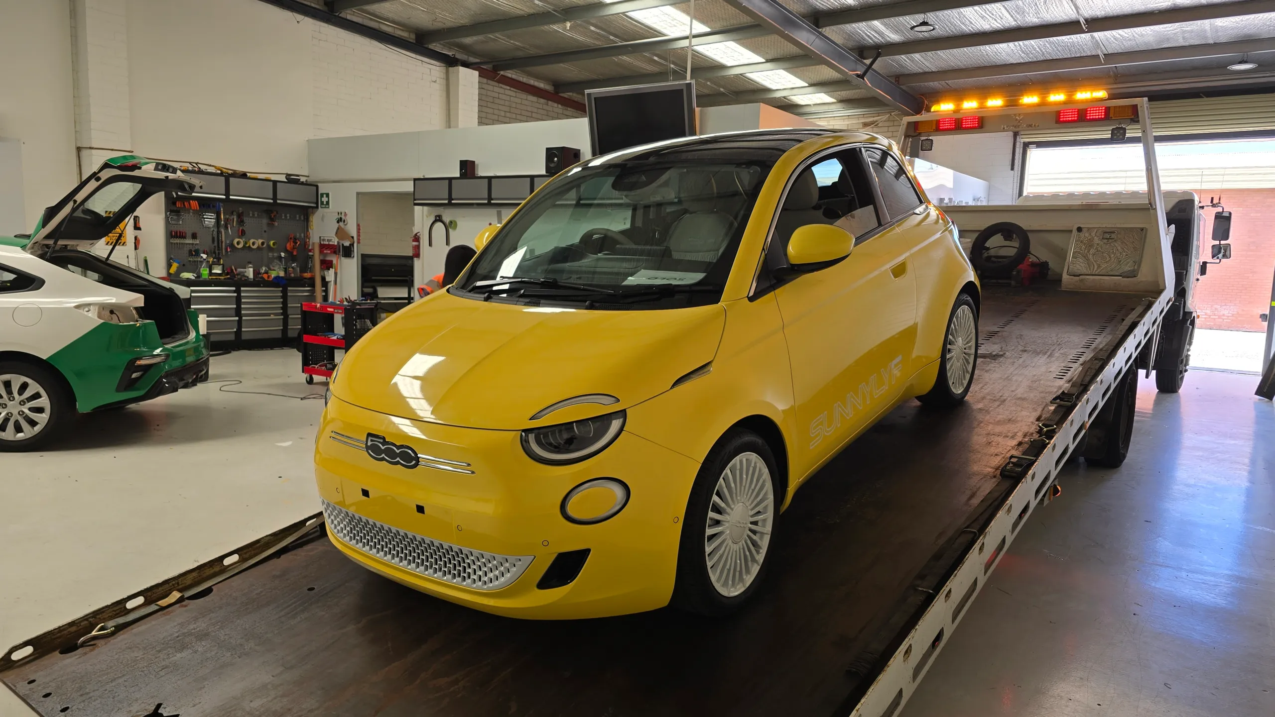 Yellow Fiat 500e front quarter on the recovery truck in the workshop