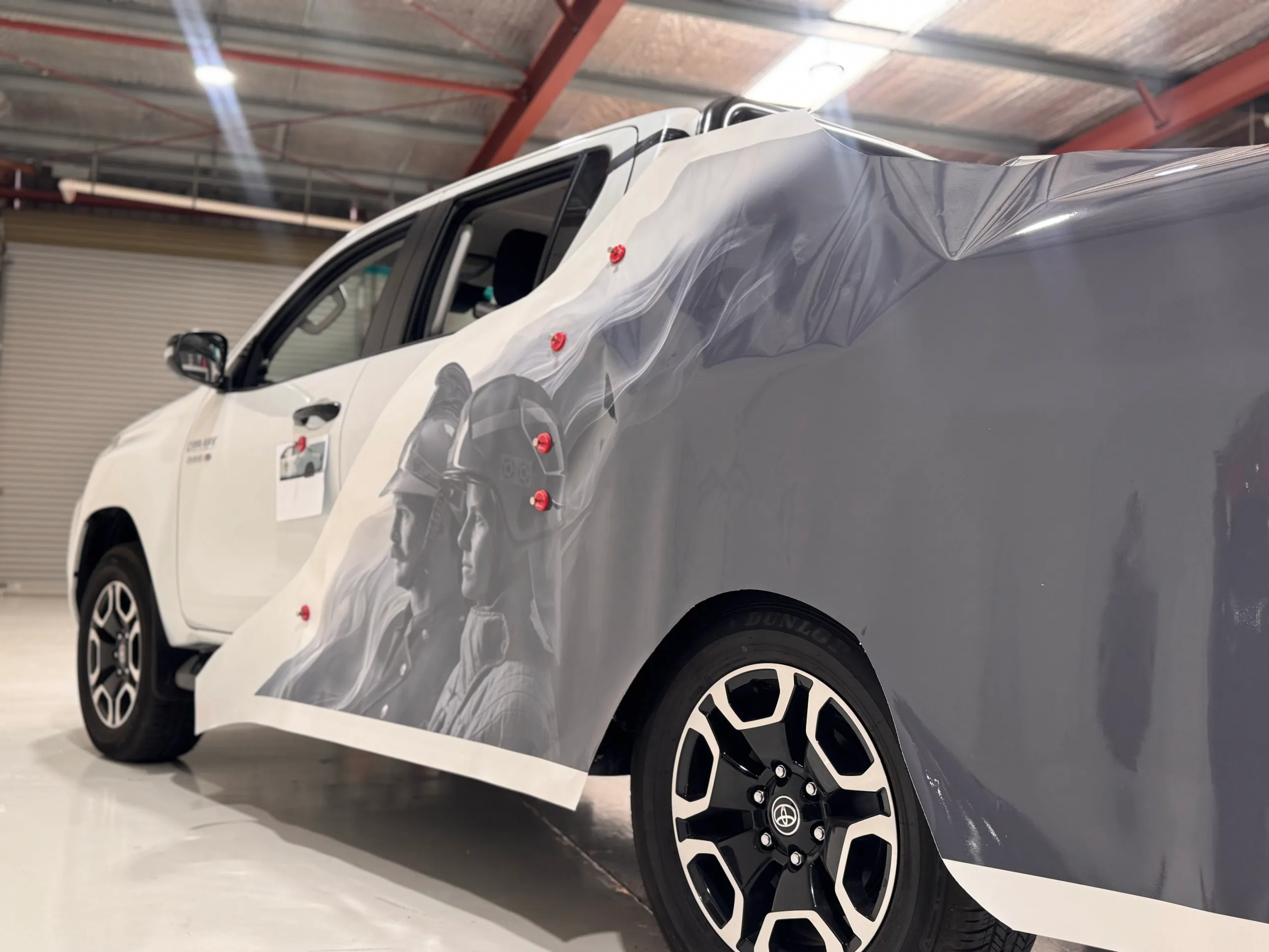 Grey firefighter artwork held against the Hilux rear quarter during wrap installation