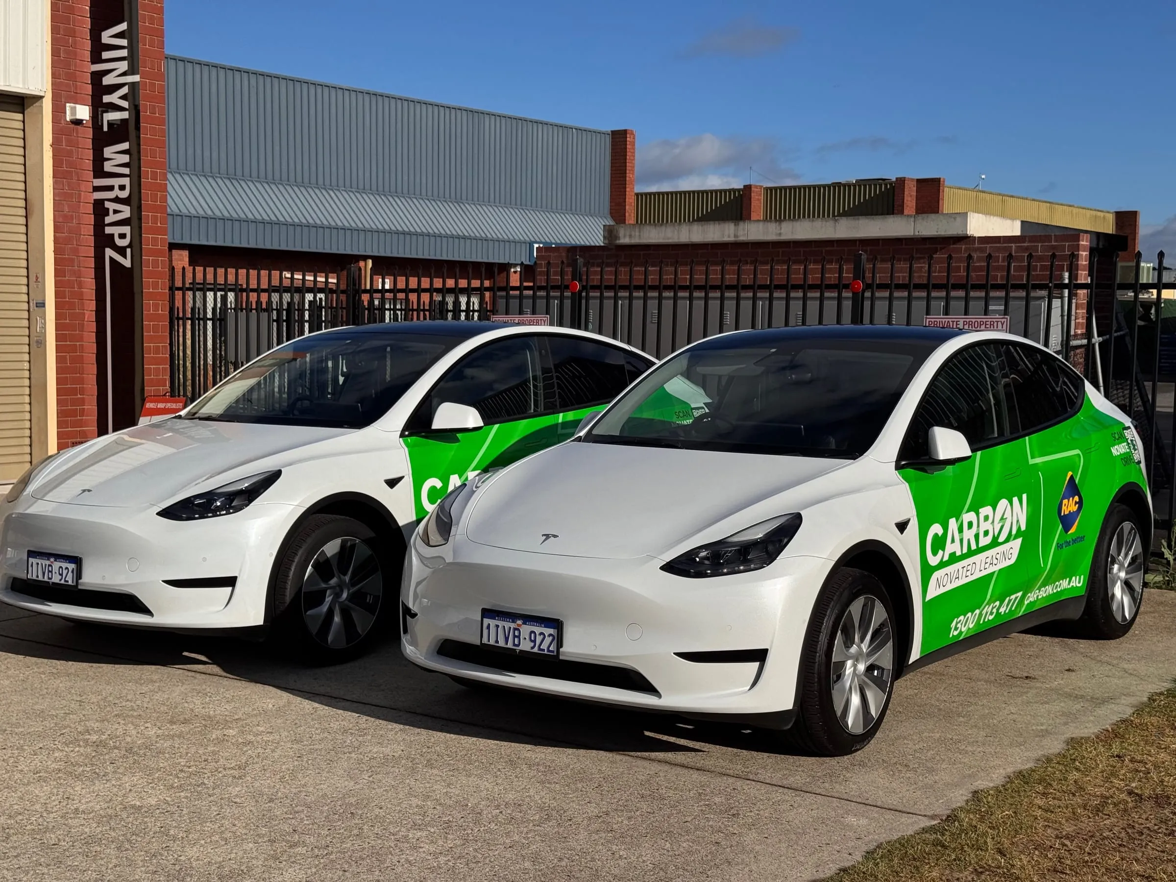 Two white CarBon Novated Leasing Teslas with matching green partial fleet wraps outside the Vinyl Wrapz workshop