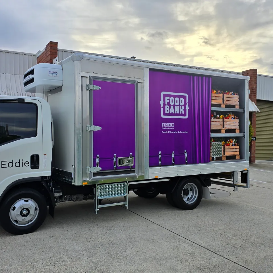 White Foodbank refrigerated truck outside the workshop, with purple branding and produce graphics on its box body