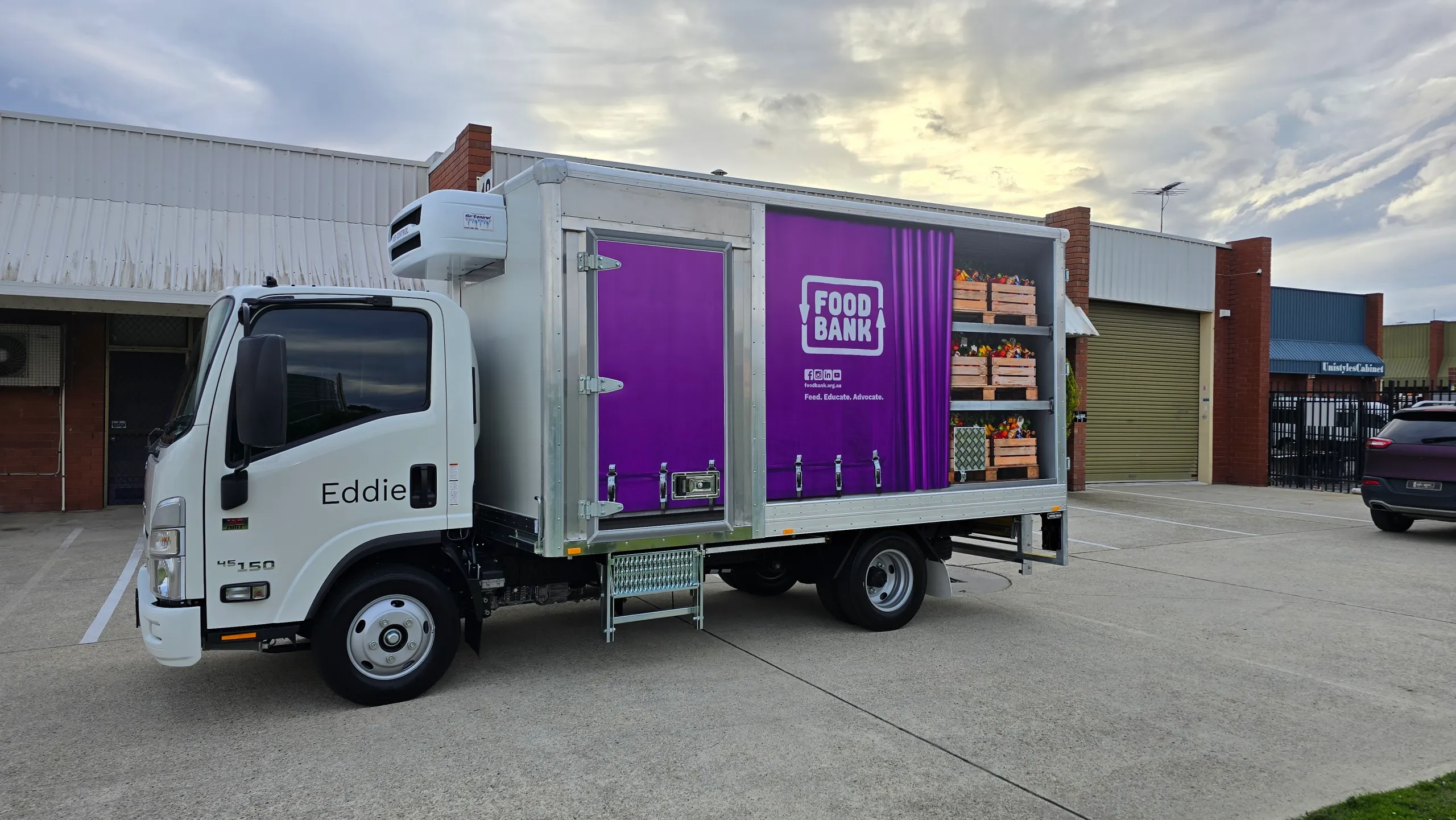 White Foodbank refrigerated truck outside the workshop, with purple branding and produce graphics on its box body