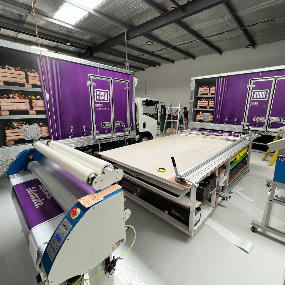 Foodbank trucks inside the workshop beside a laminating table and printing equipment