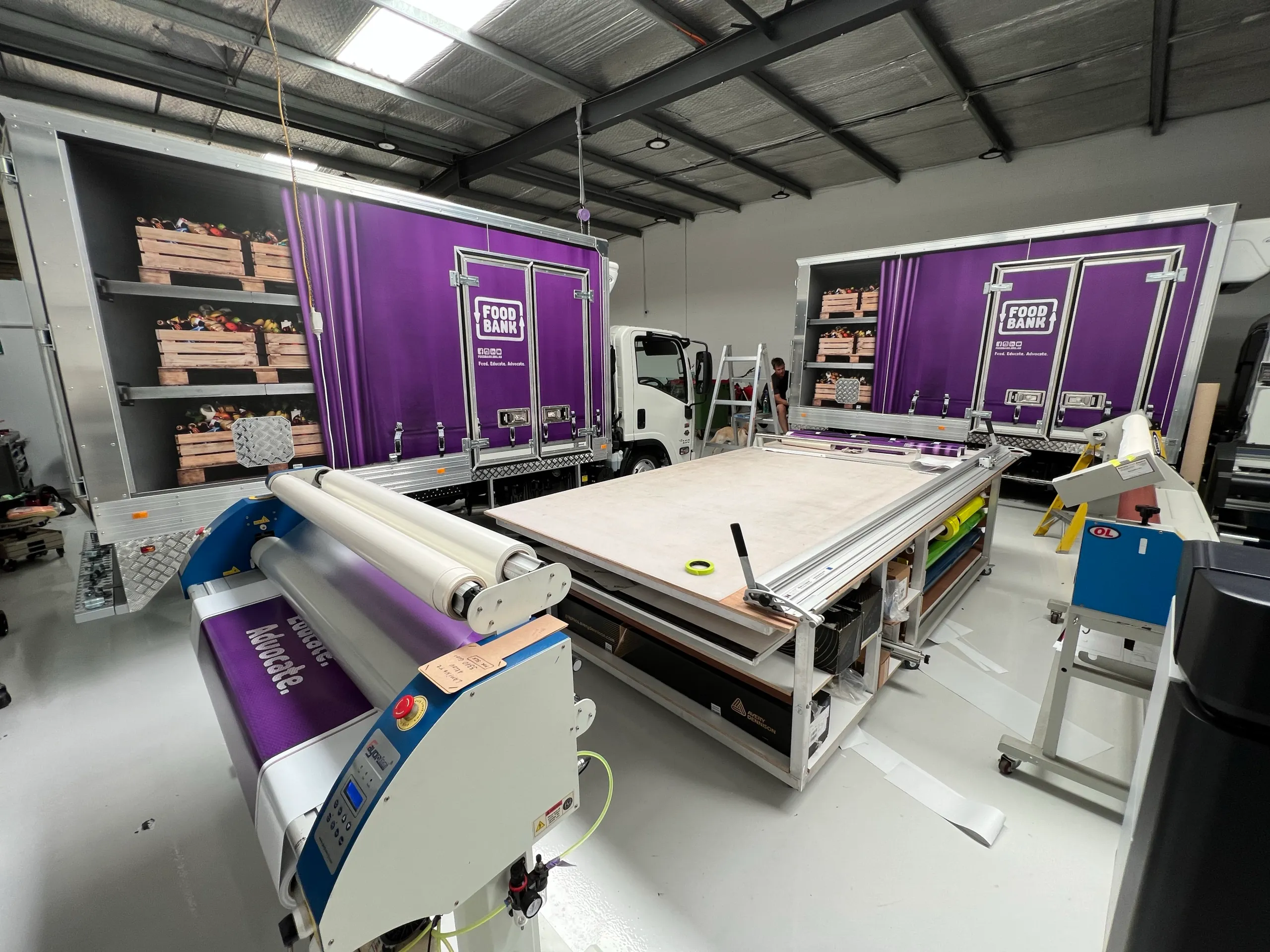 Foodbank trucks inside the workshop beside a laminating table and printing equipment