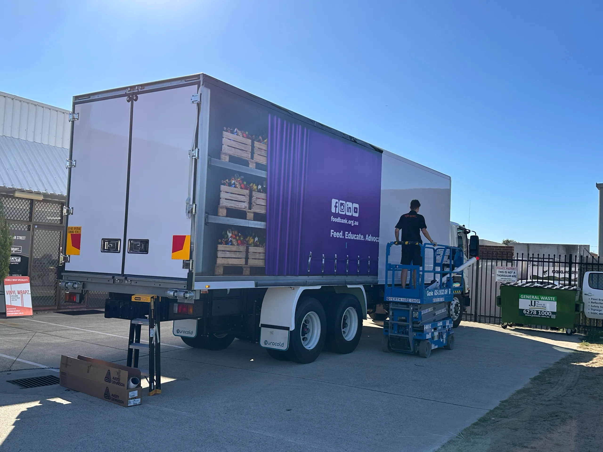 Installer facing away on a scissor lift beside partly fitted Foodbank truck graphics