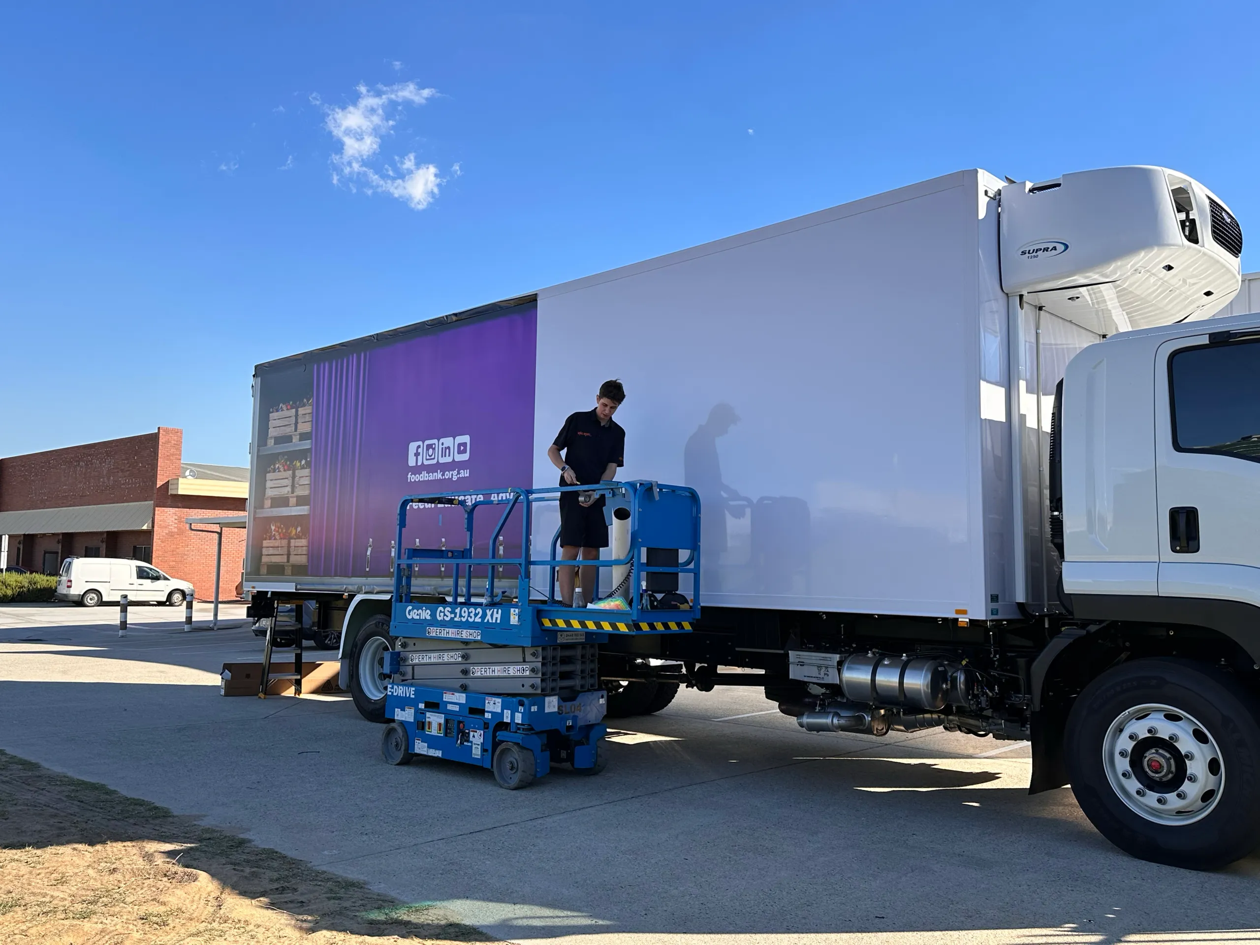 Installer on a scissor lift beside the refrigerated truck during Foodbank graphics fitting