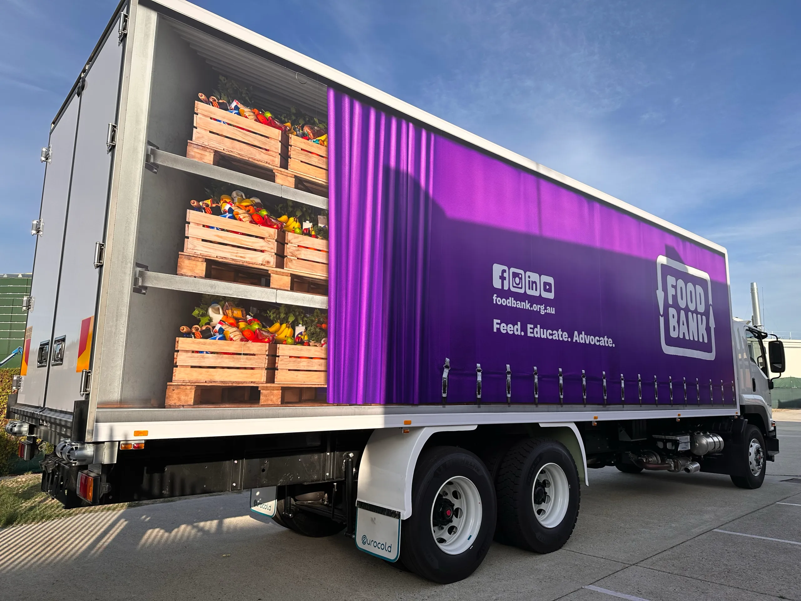 Foodbank refrigerated truck with purple graphics and printed produce crates viewed from the rear quarter