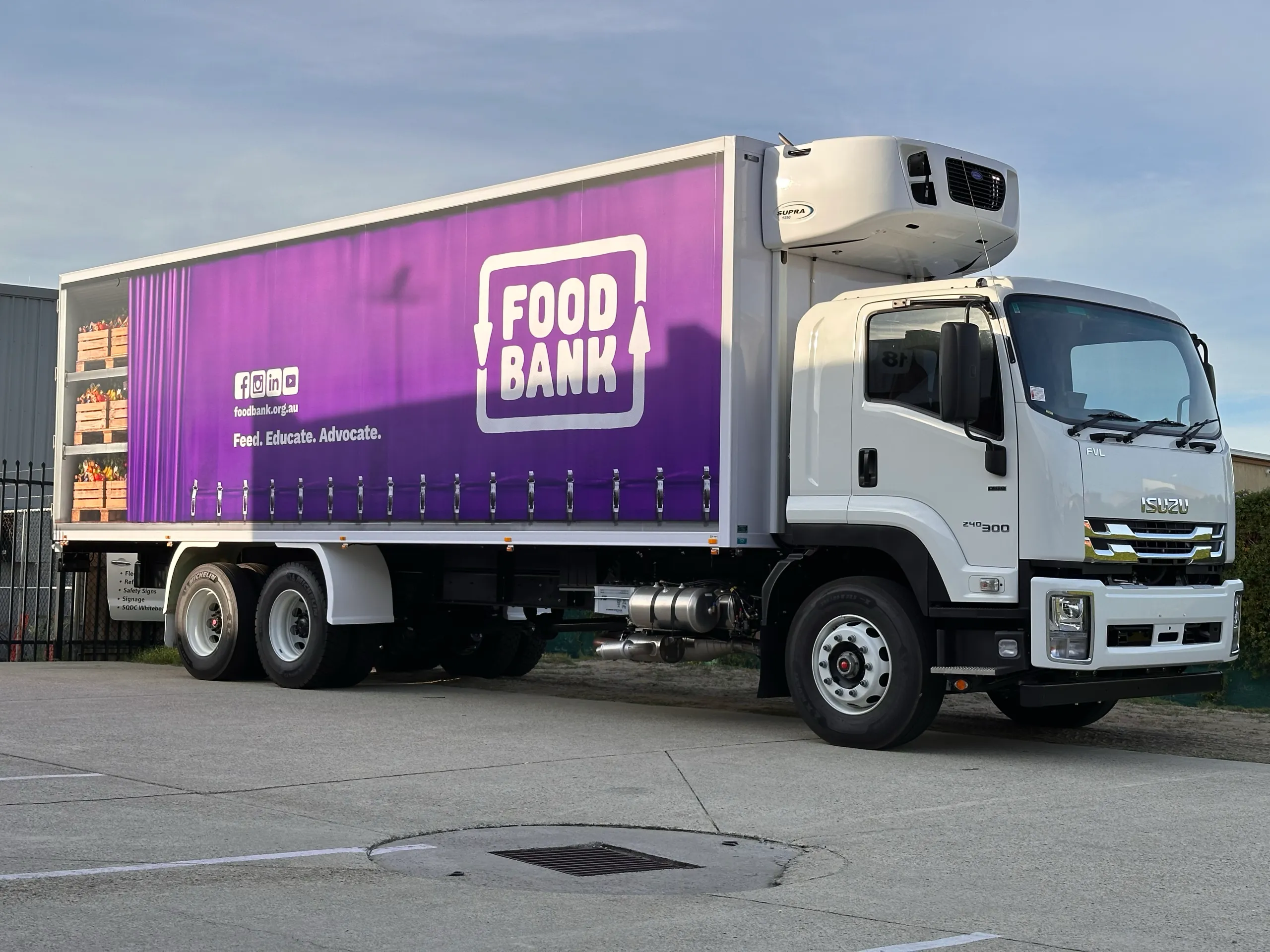 White Isuzu refrigerated truck with purple Foodbank graphics outside the workshop