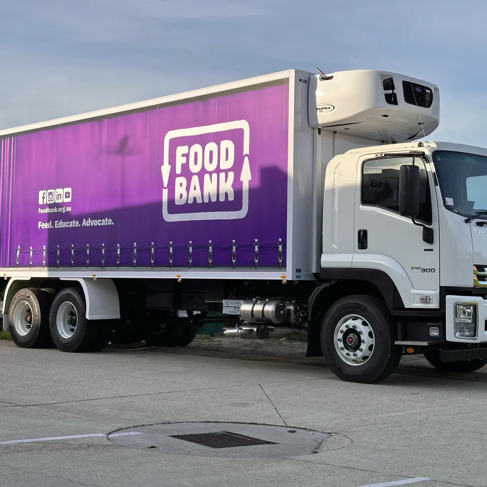 White Isuzu refrigerated truck with purple Foodbank graphics outside the workshop