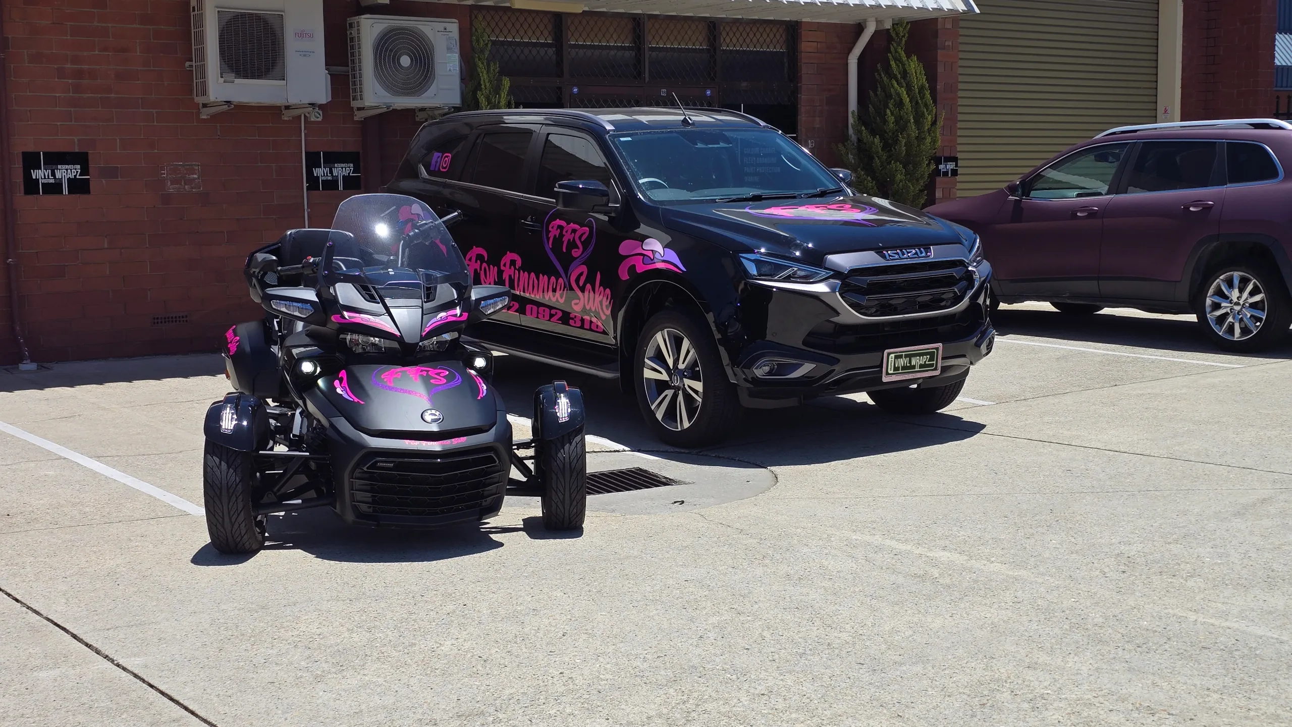 For Finance Sake Can-Am Spyder and Isuzu MU-X with matching pink graphics outside the workshop