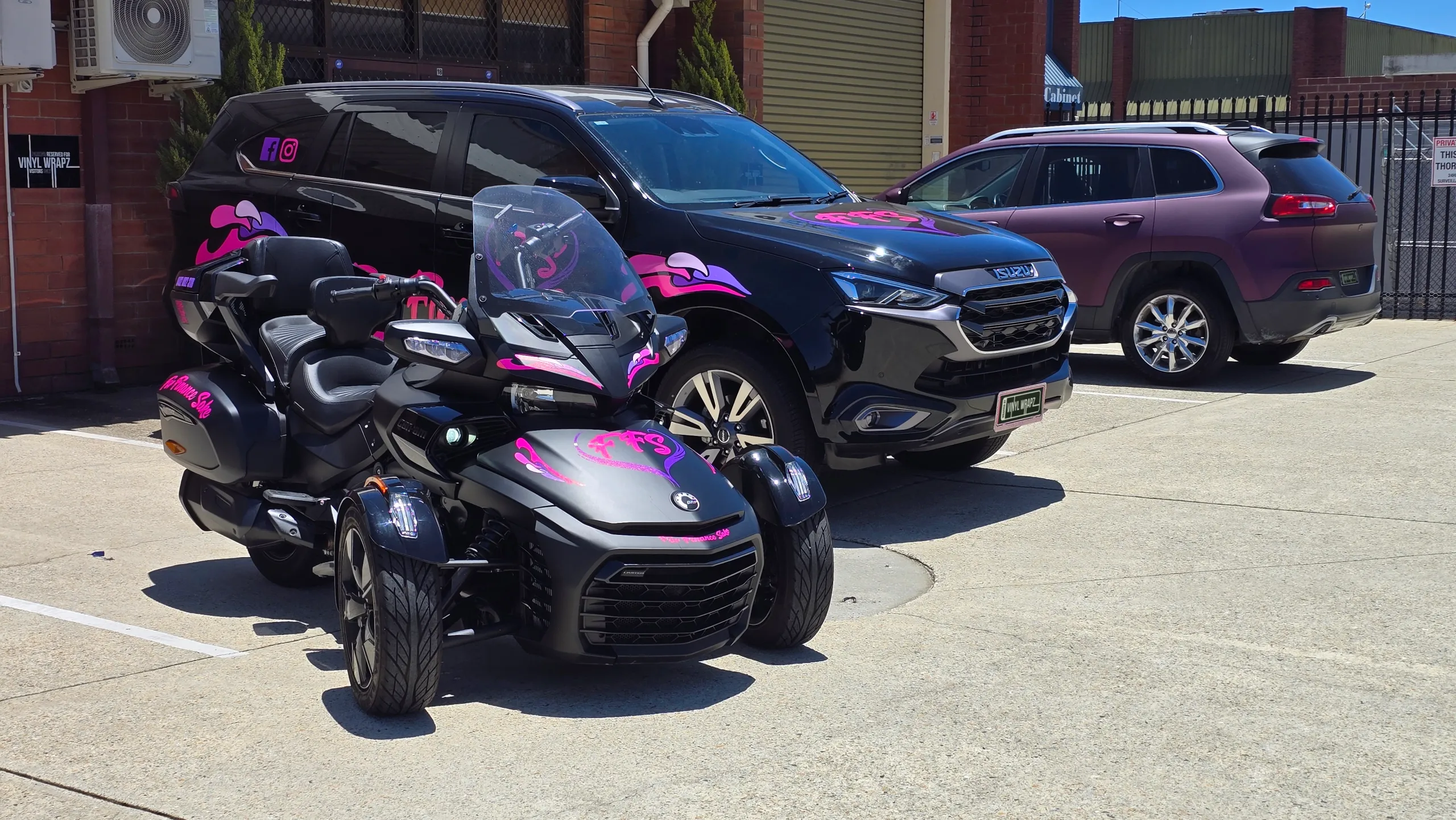 Can-Am Spyder with pink For Finance Sake graphics parked in front of the matching Isuzu MU-X