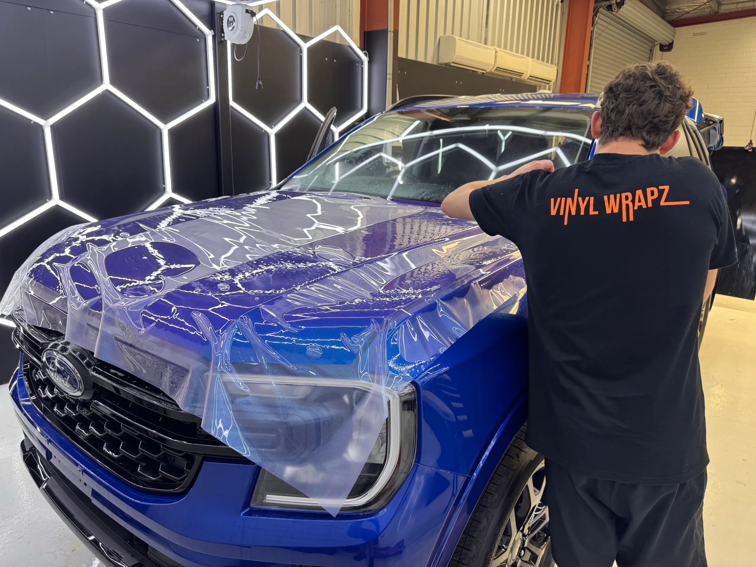 Installer facing away while fitting clear film to a blue Ford Everest bonnet