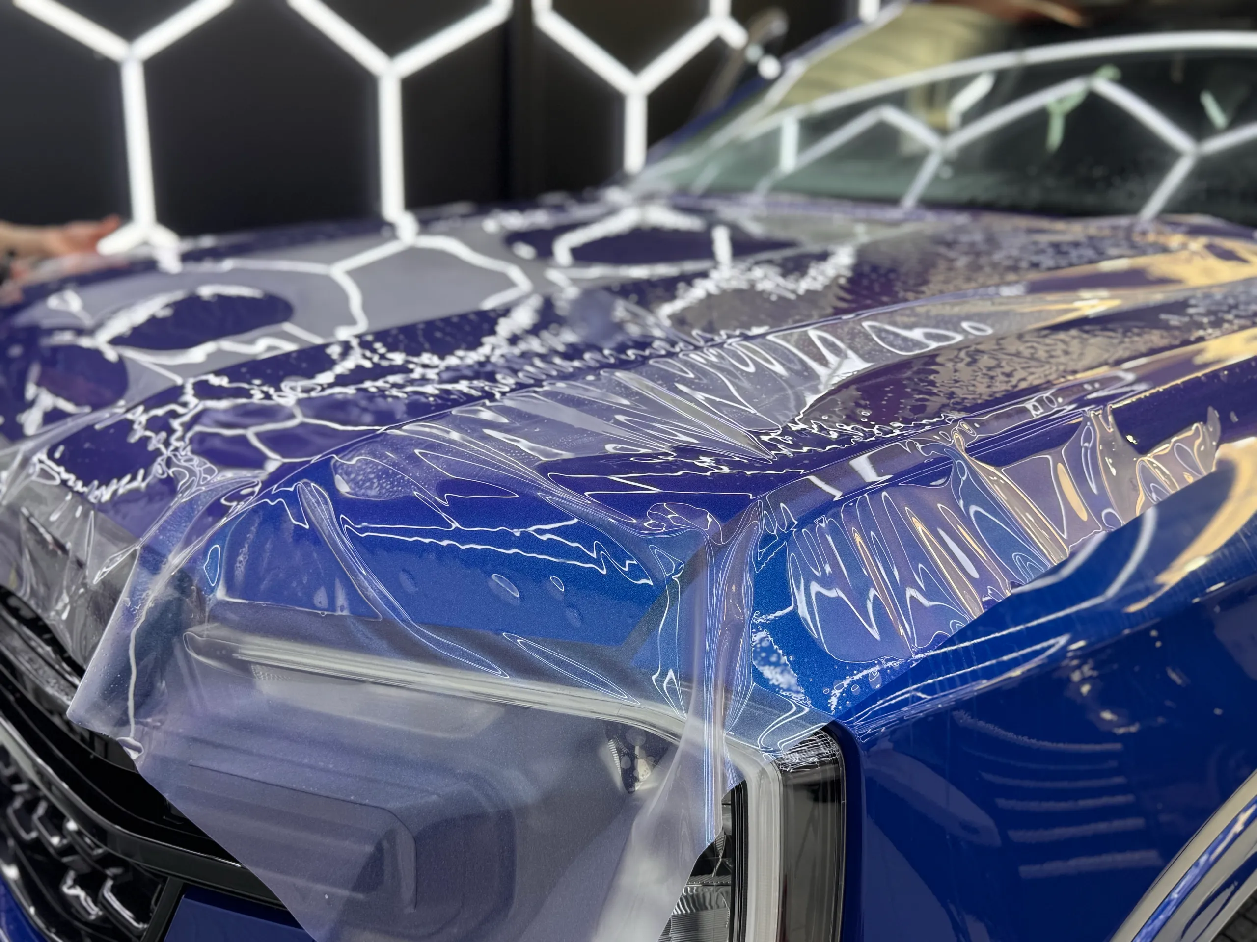 Wet clear film across the blue Ford Everest bonnet and headlight during installation