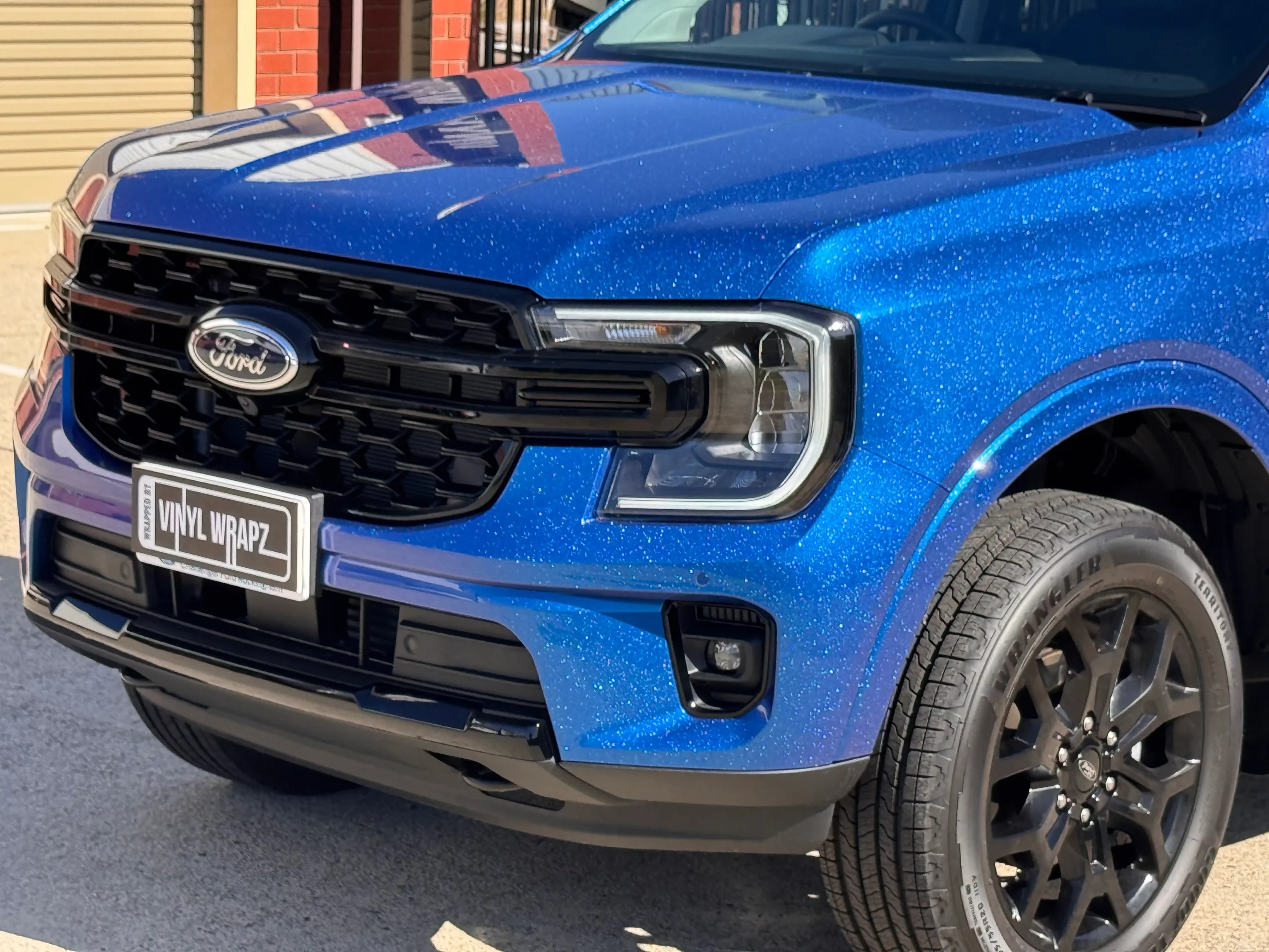 Iridescent blue Ford Everest grille, headlight and front wheel outside the workshop