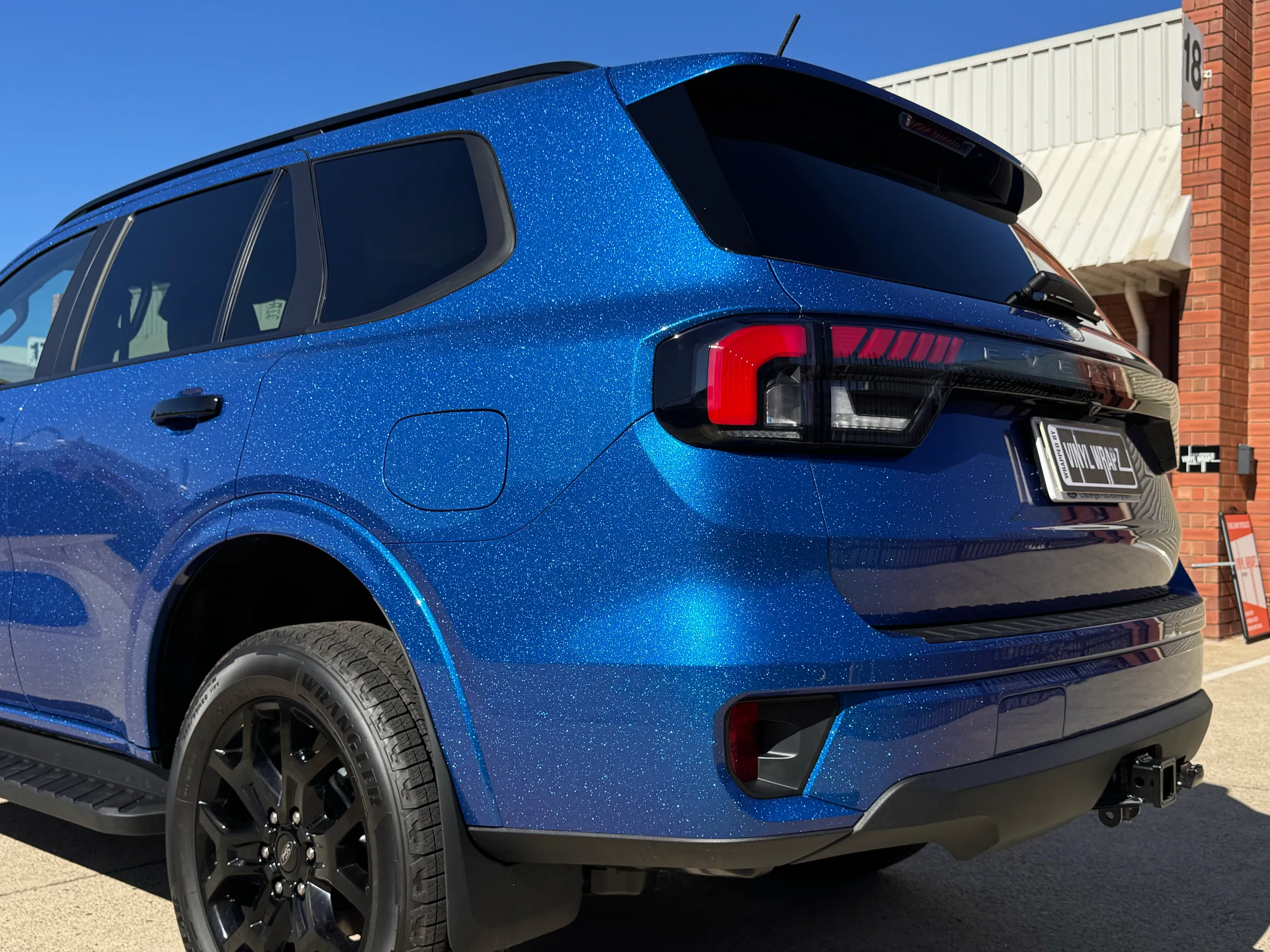 Iridescent blue Ford Everest rear quarter beneath dark windows and a black roof spoiler