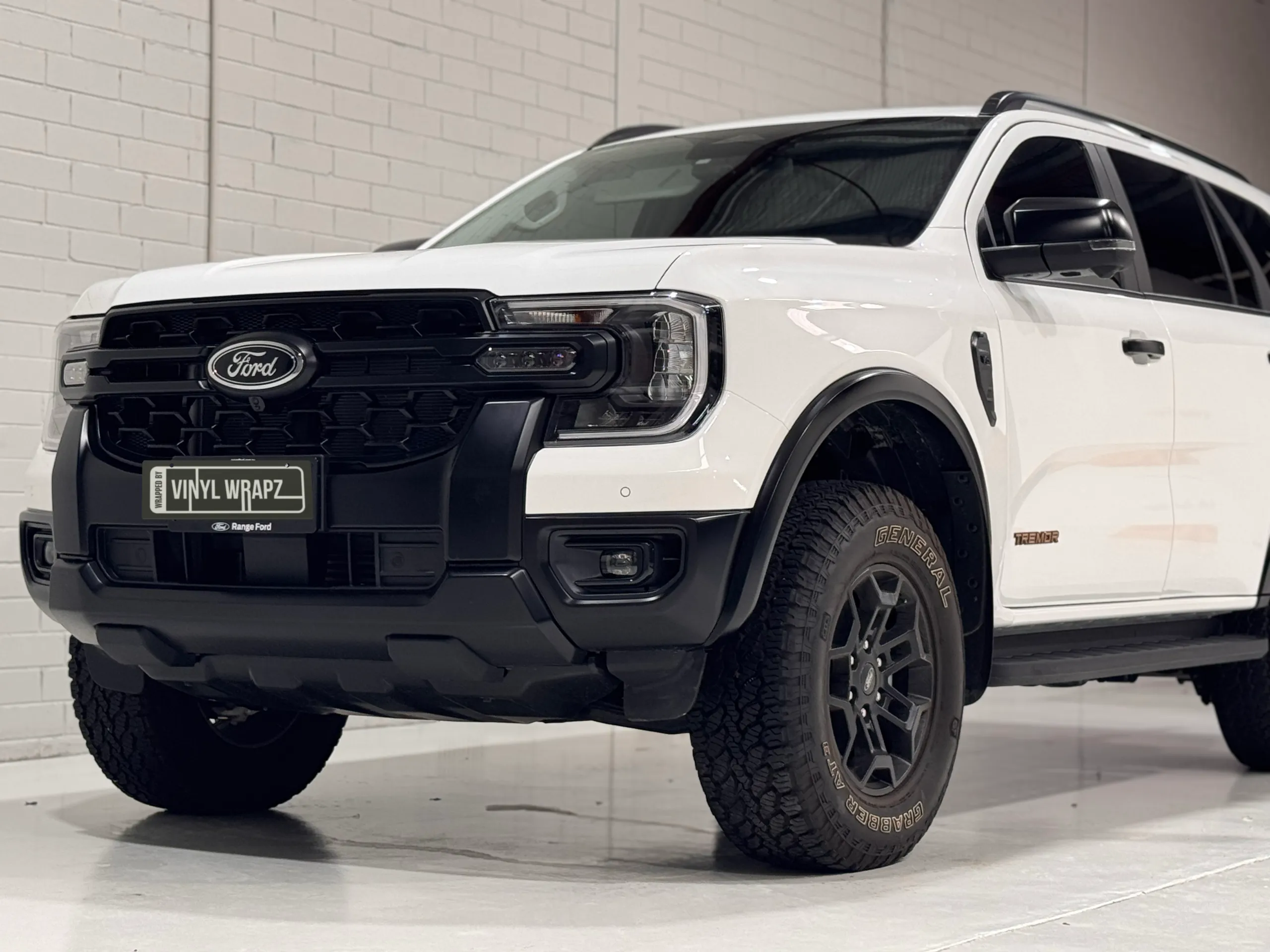 Low-angle view of a white Ford Everest Tremor grille, front bumper and wheel