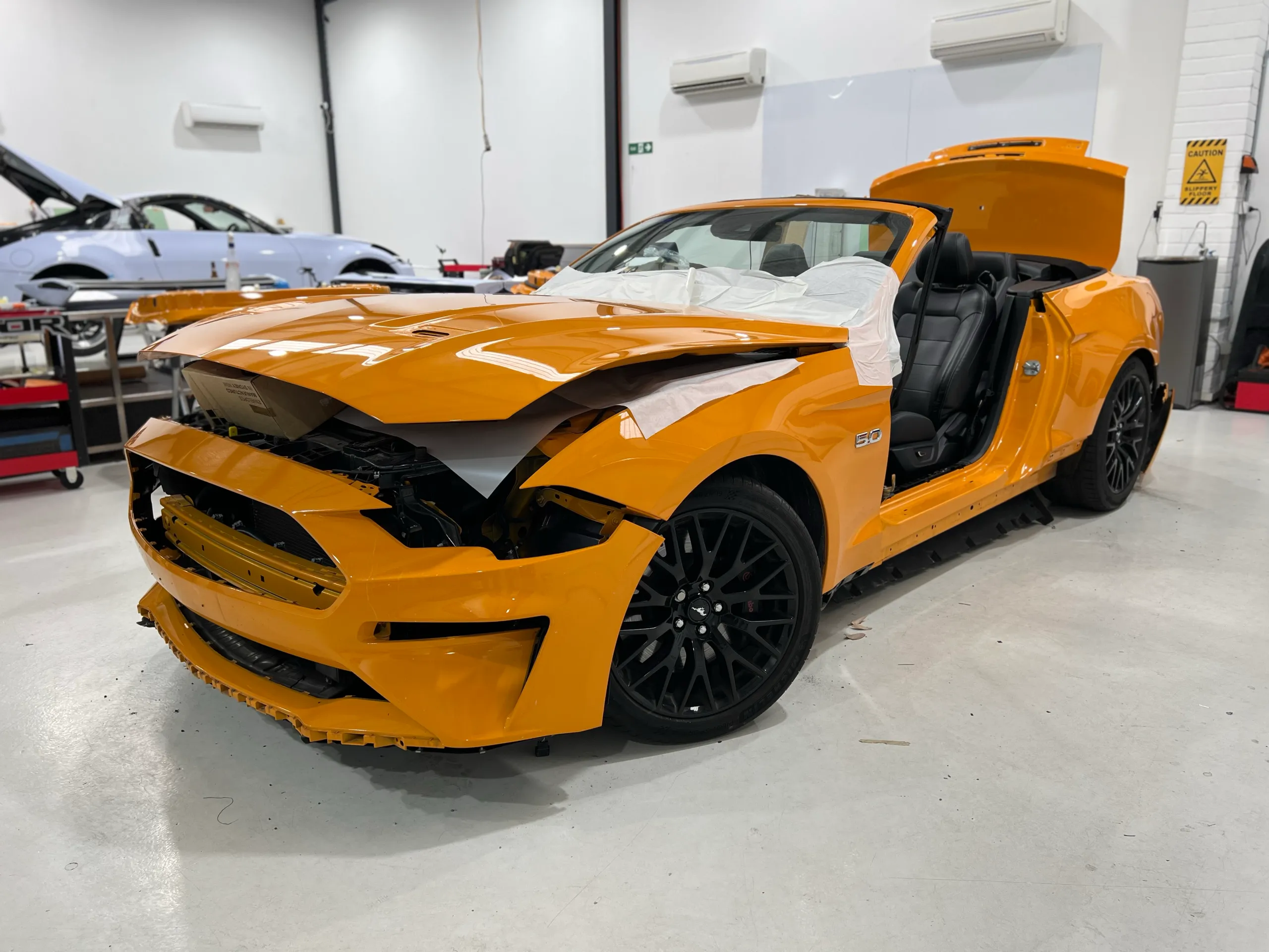Orange Ford Mustang convertible dismantled for wrapping, front quarter in the workshop