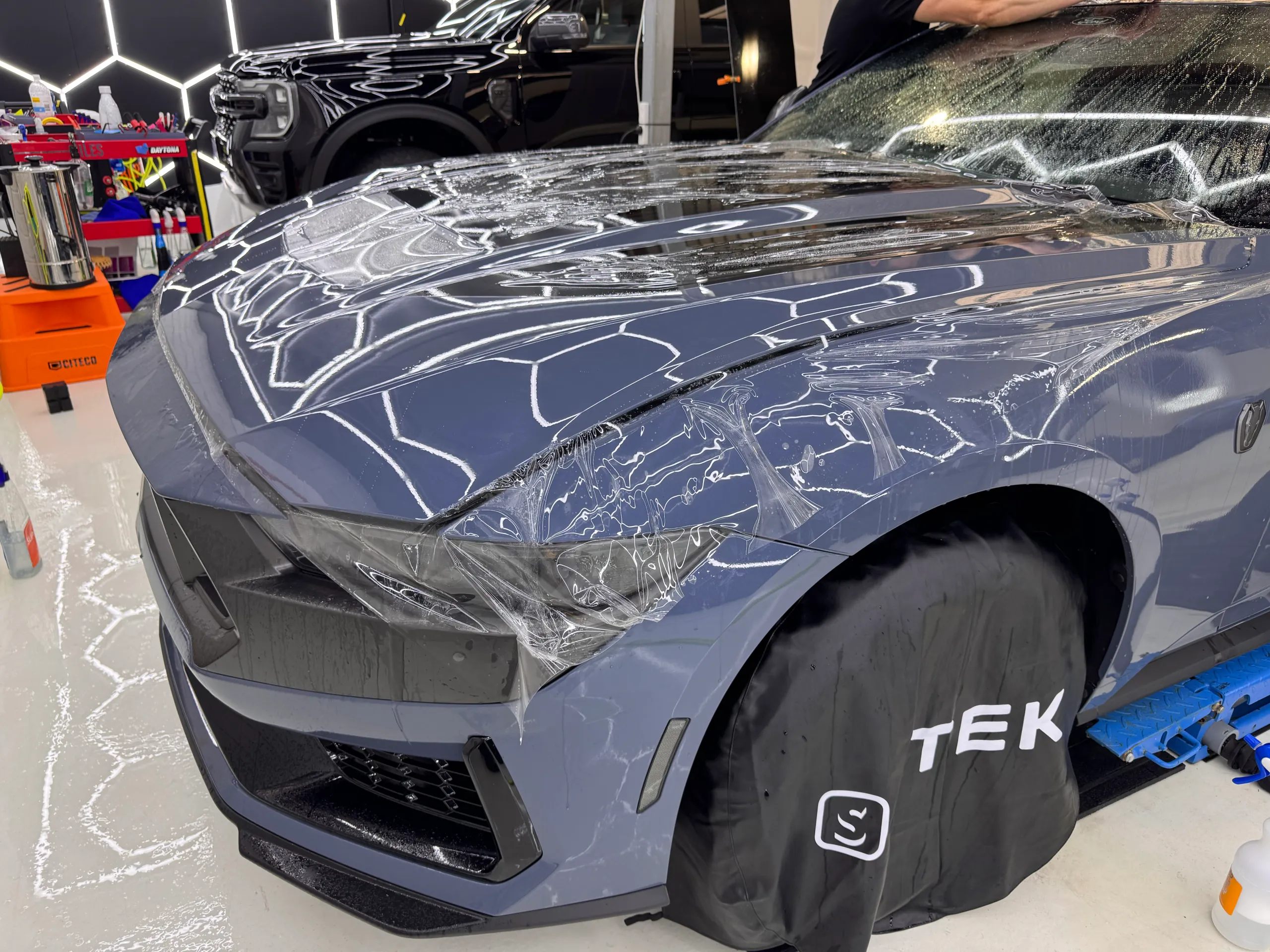 Clear film being fitted over the blue-grey Ford Mustang Dark Horse bonnet and front guard