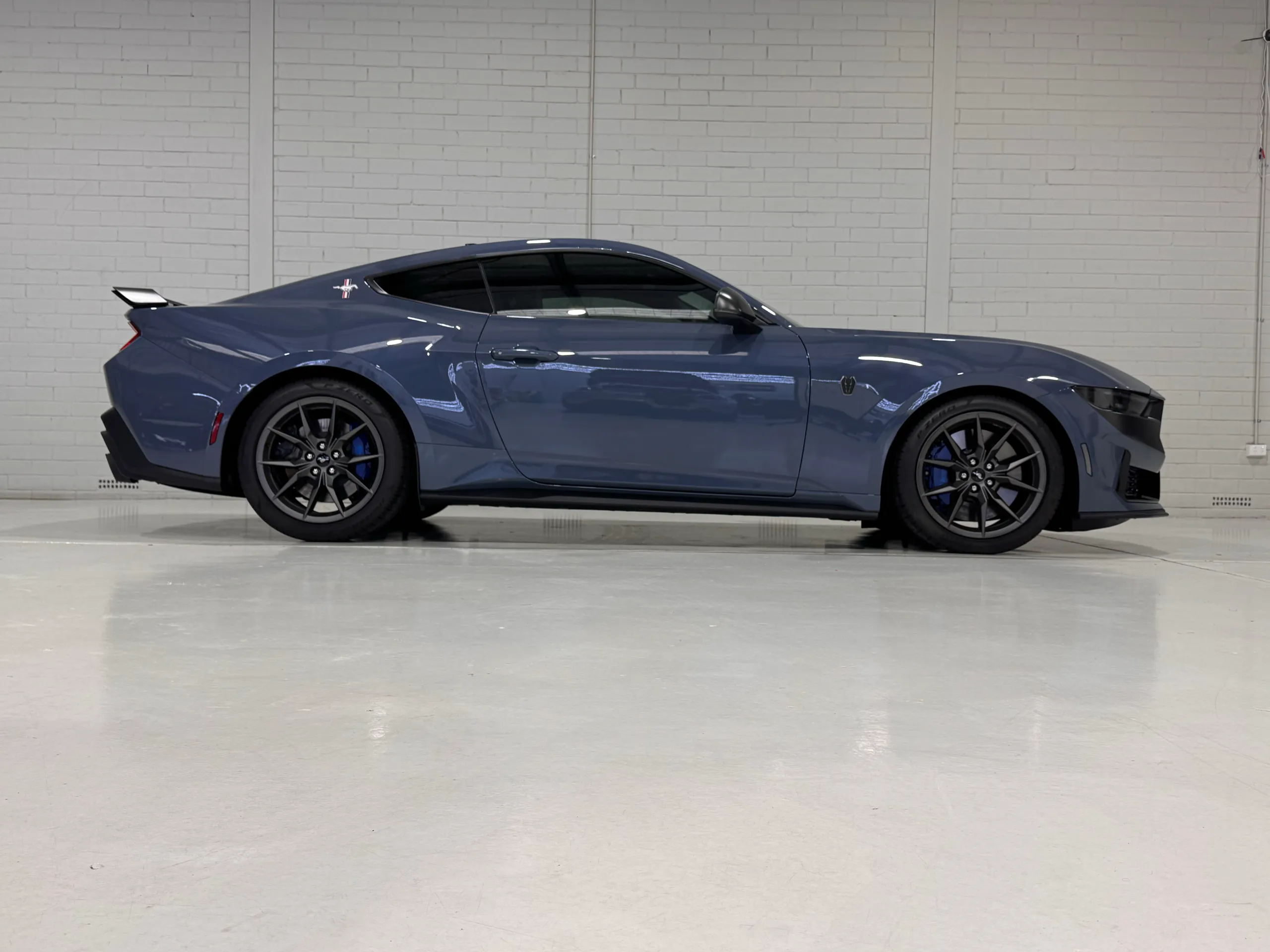 Side view of a gloss blue-grey Ford Mustang Dark Horse against a white workshop wall