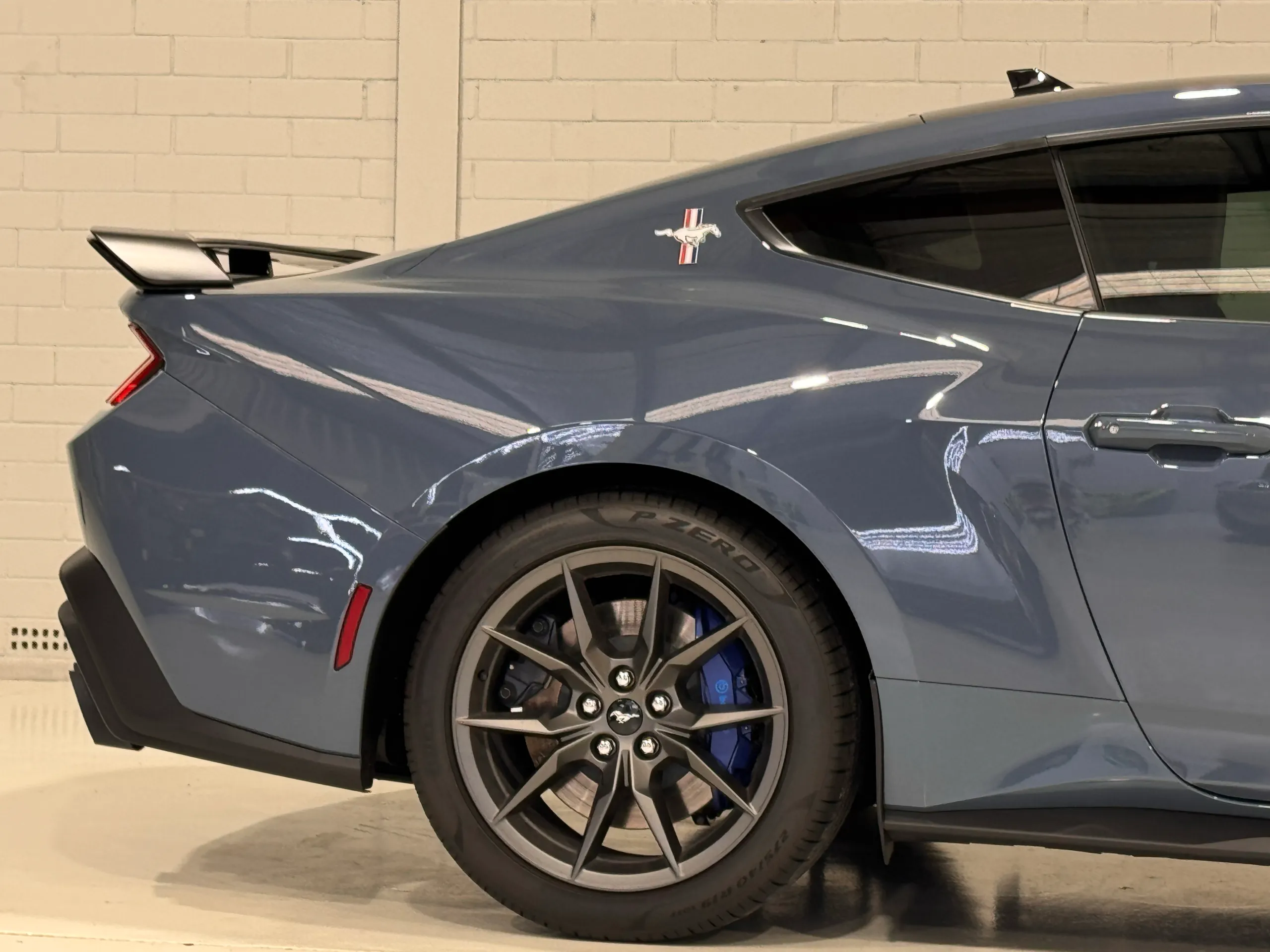 Gloss blue-grey Ford Mustang Dark Horse rear quarter, wheel and spoiler in the workshop