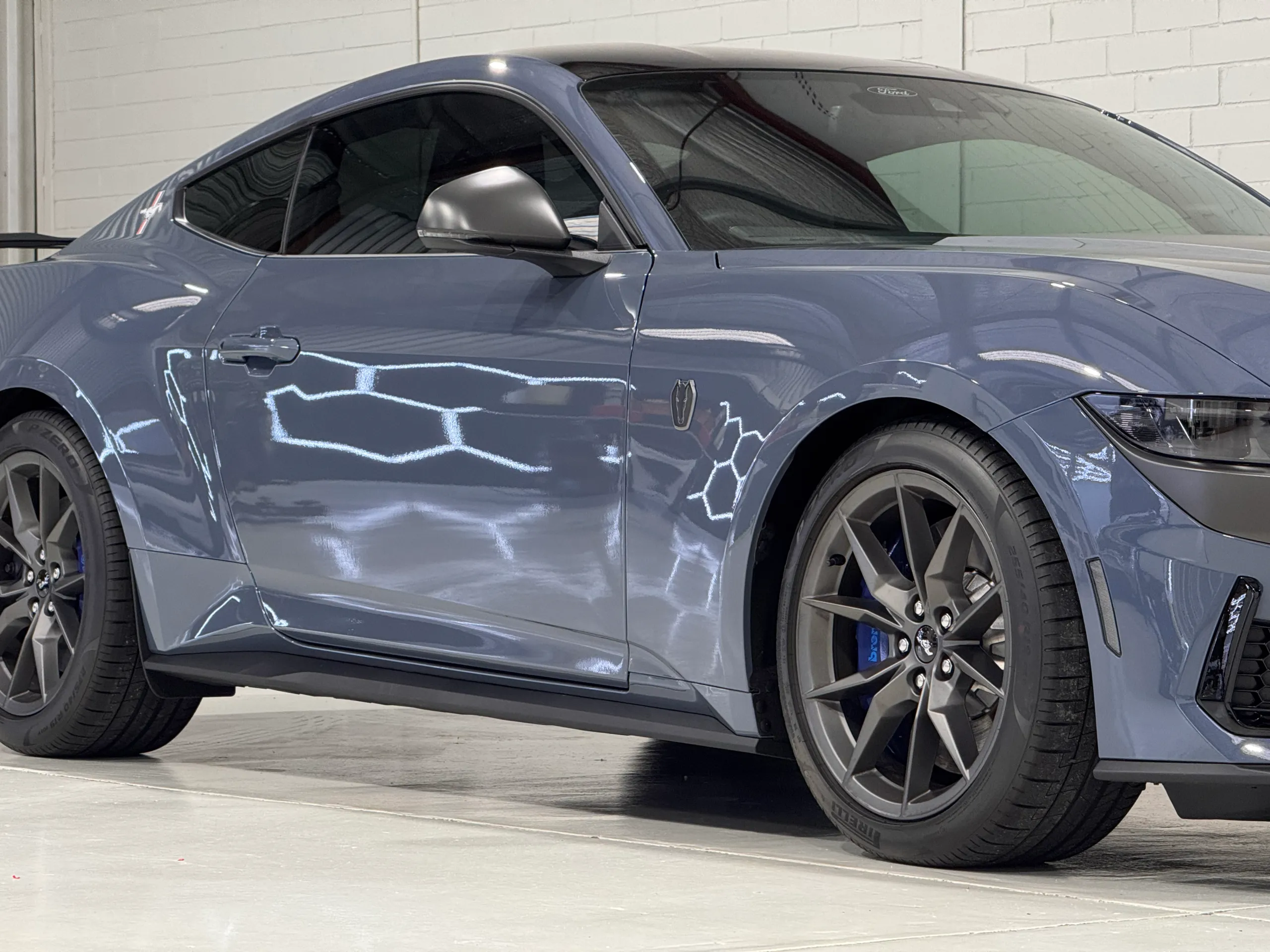 Gloss blue-grey Ford Mustang Dark Horse door and front wheel reflecting workshop lights