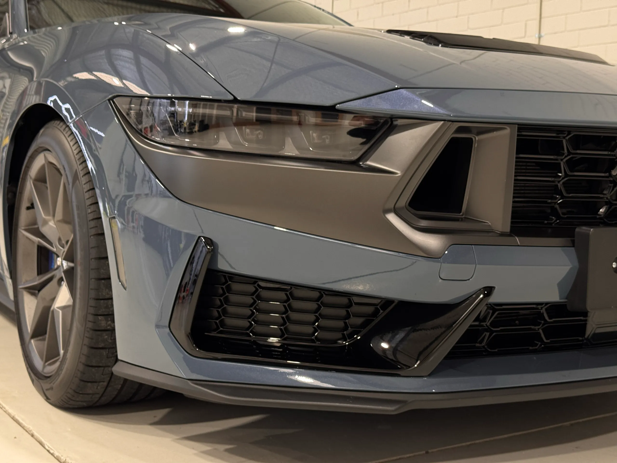 Ford Mustang Dark Horse headlight, grille and front bumper reflecting workshop lights