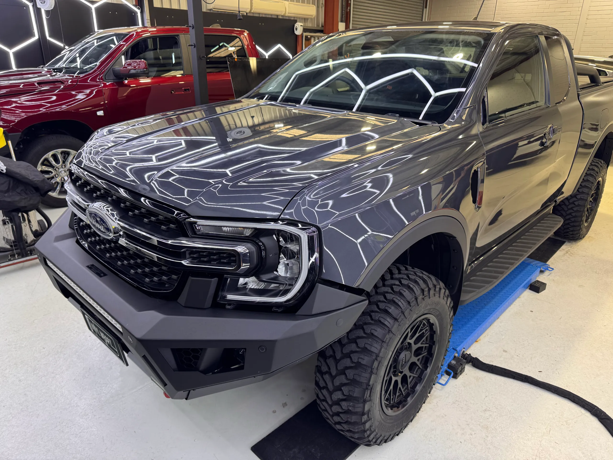 Gloss grey Ford Ranger front end and cab on a workshop lift, with ceiling lights reflected across the bonnet