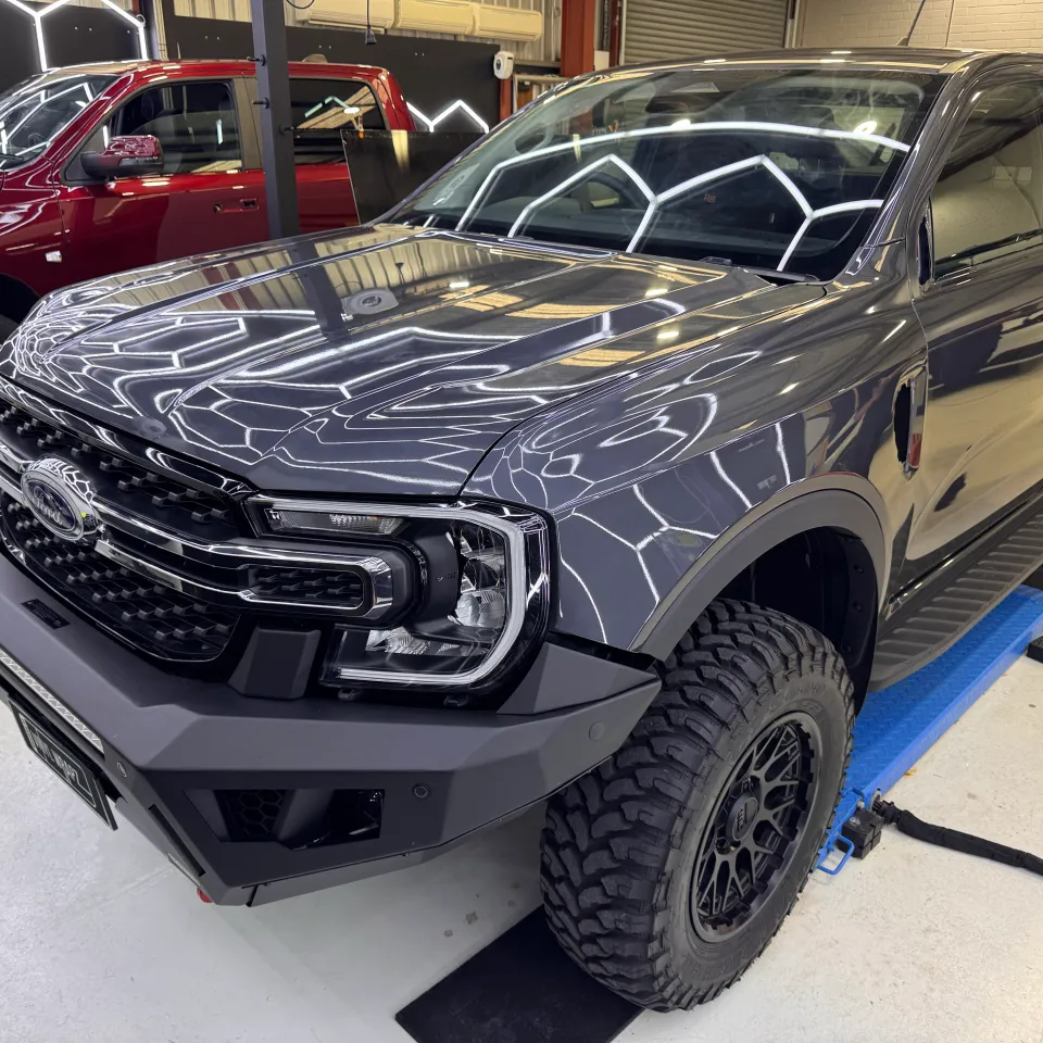 Gloss grey Ford Ranger front end and cab on a workshop lift, with ceiling lights reflected across the bonnet