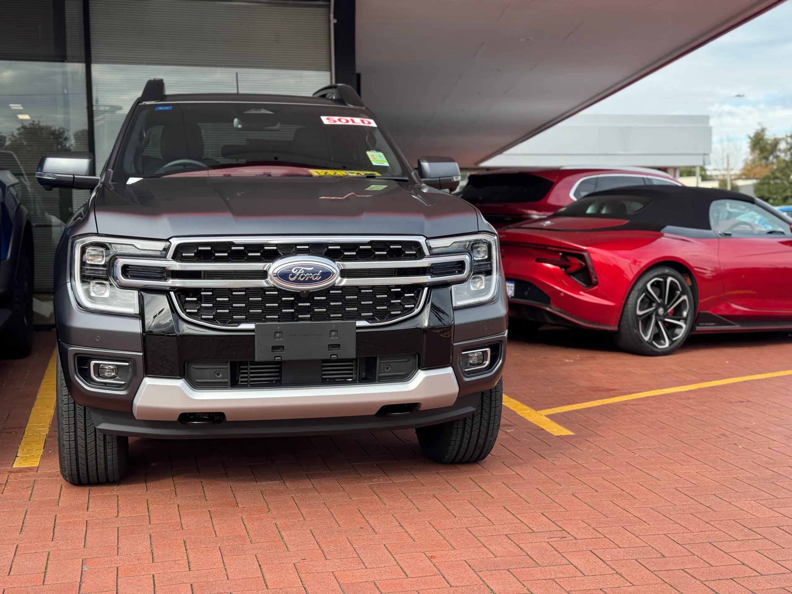 Front view of a satin grey Ford Ranger Platinum at a dealership, beside a red convertible