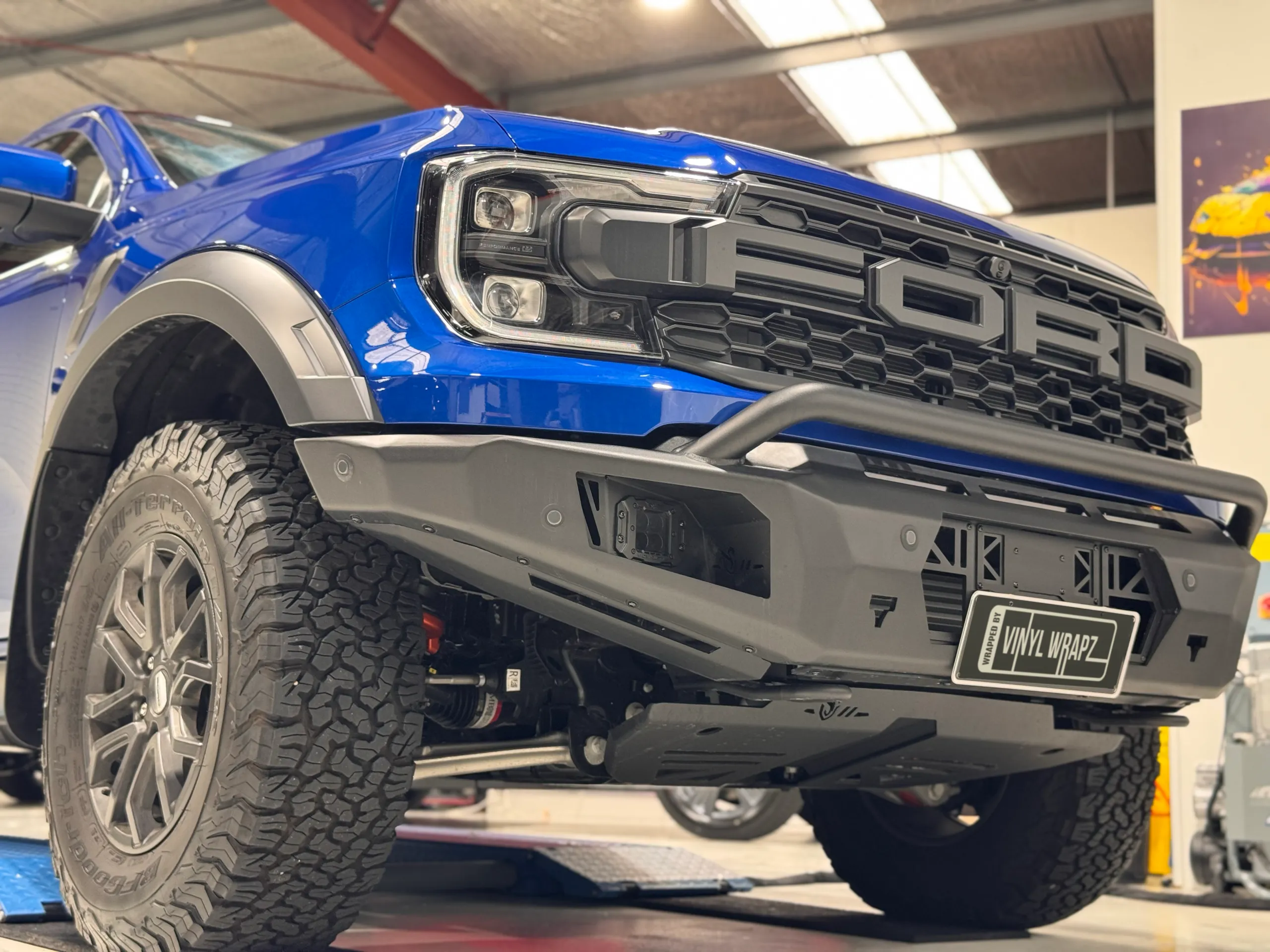Low view of the blue Ford Ranger Raptor grille, black front bar and front wheel