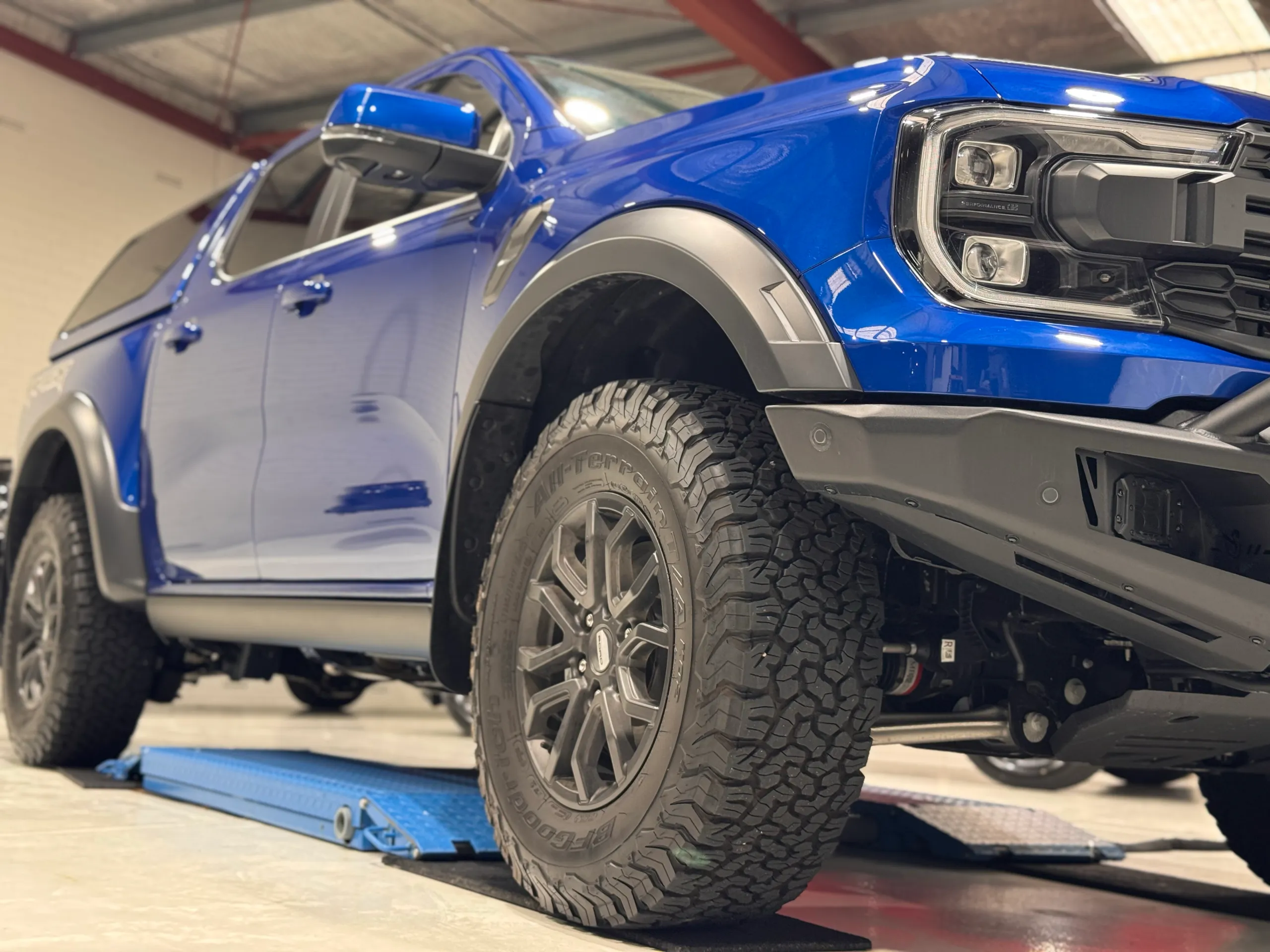 Blue Ford Ranger Raptor front wheel and guard viewed from below in the workshop