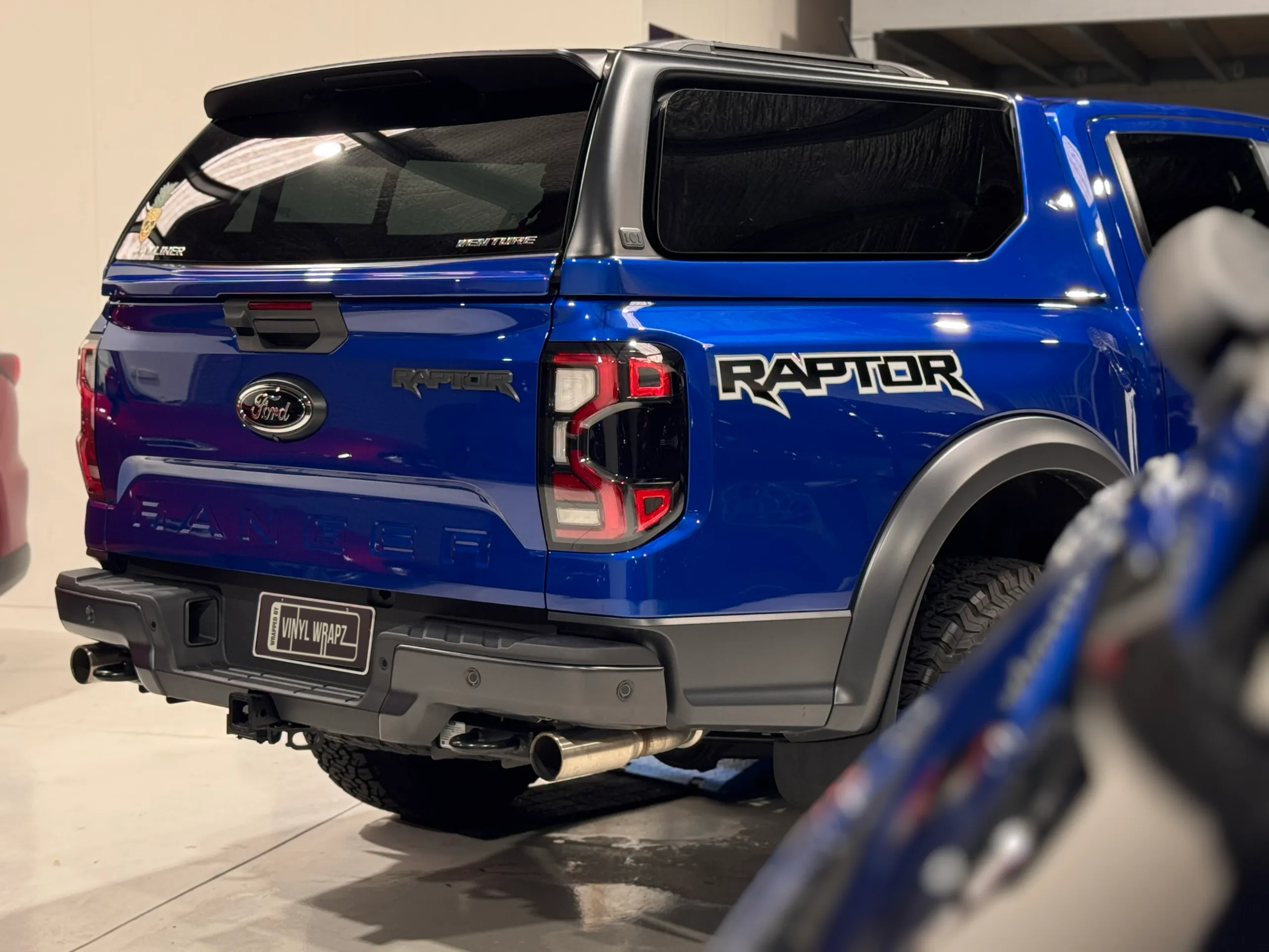 Gloss blue Ford Ranger Raptor rear quarter, partly framed by another vehicle in the foreground