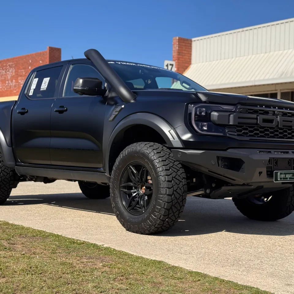 Low front-quarter view of the satin grey Ranger Raptor beside a brick workshop