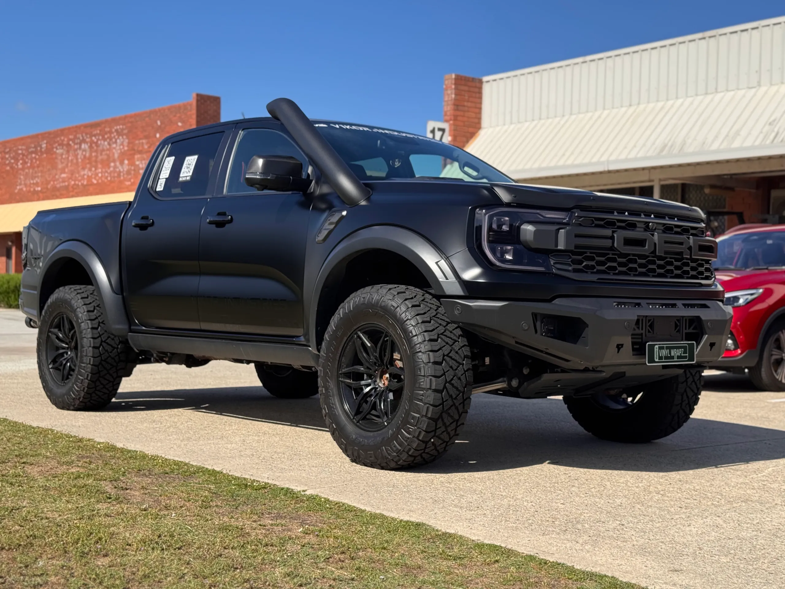 Low front-quarter view of the satin grey Ranger Raptor beside a brick workshop