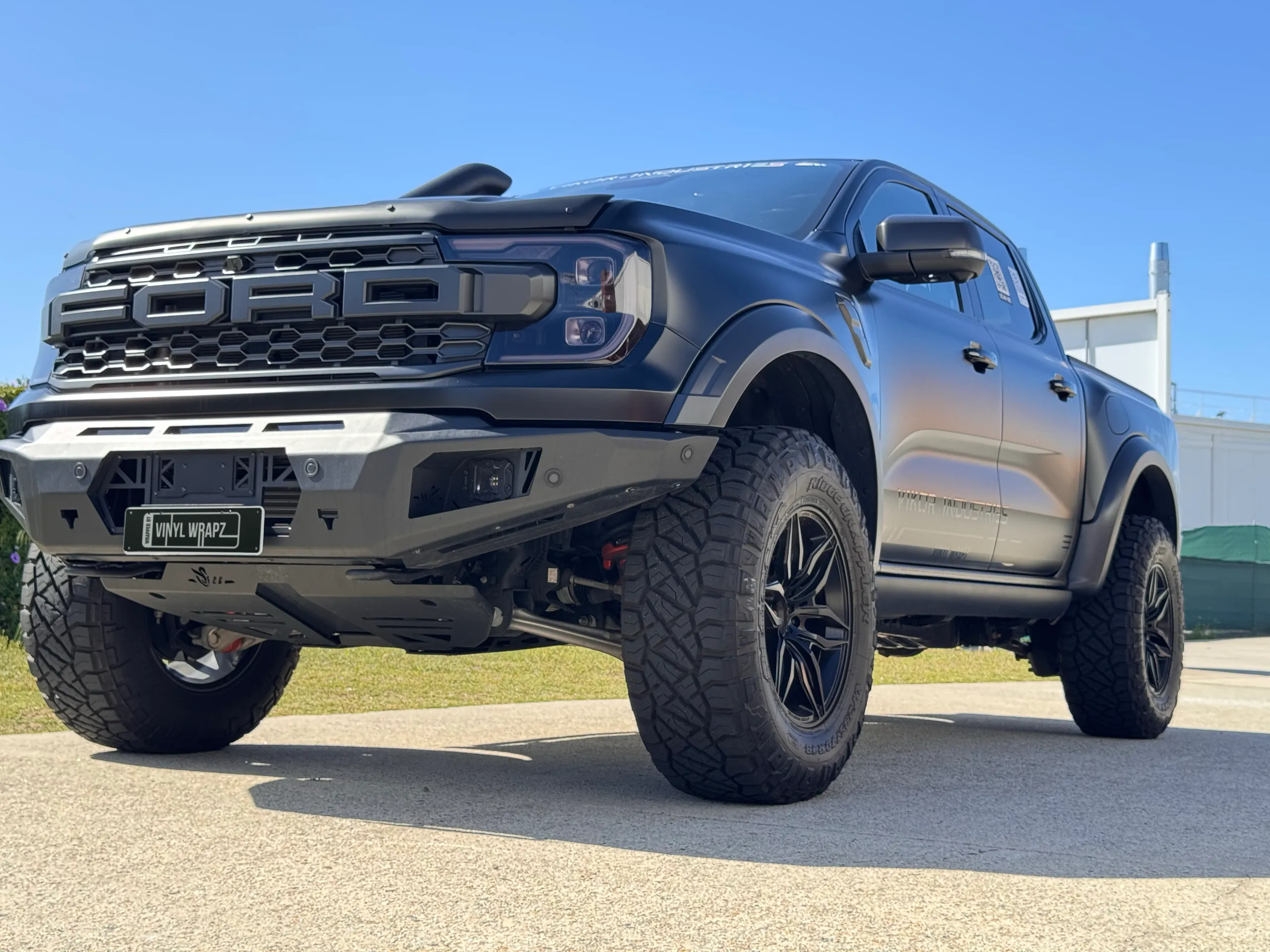 Low front-quarter view of the satin grey Ford Ranger Raptor under a blue sky