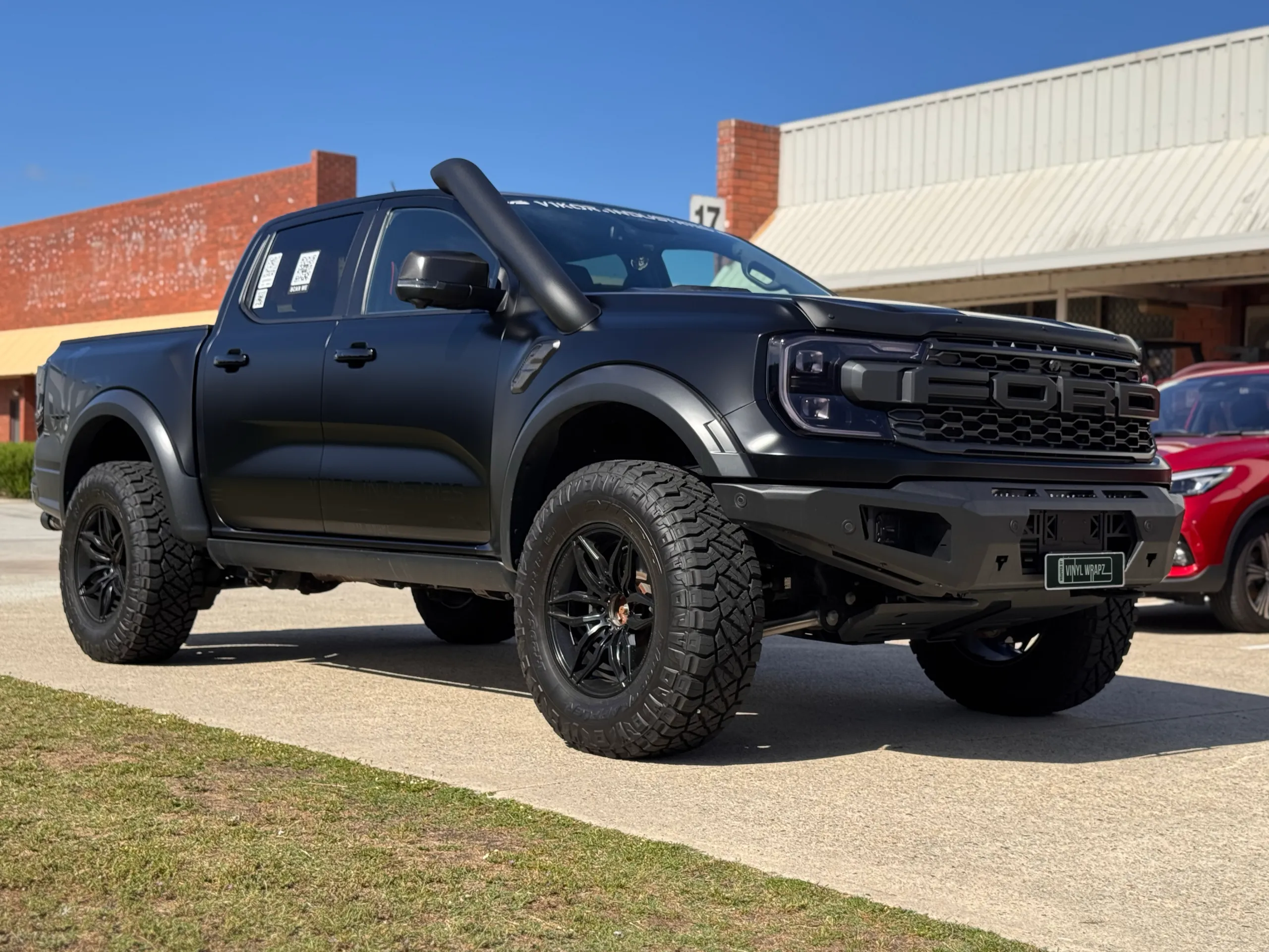 Satin grey Ranger Raptor viewed from the front quarter beside a brick building