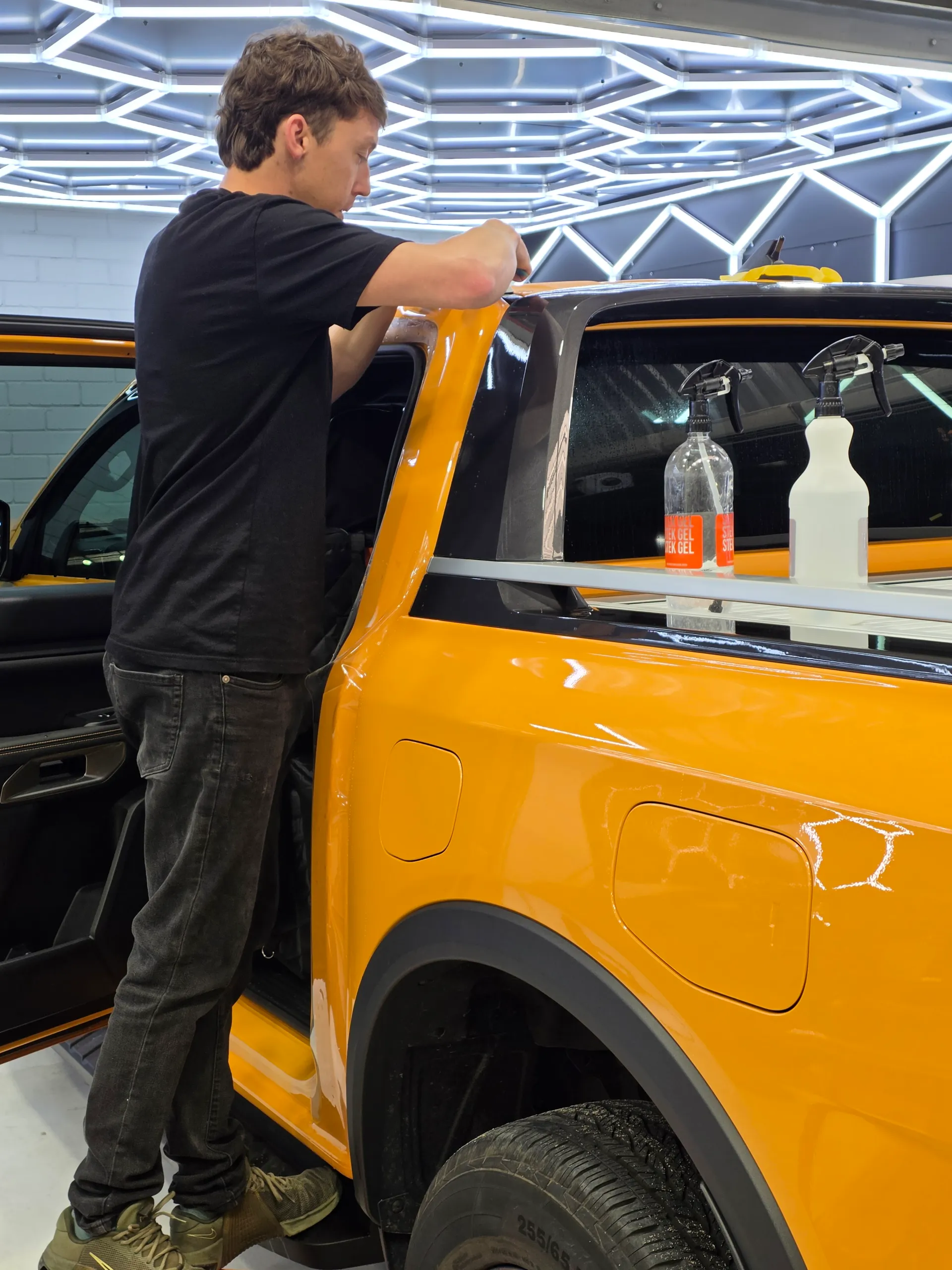 Installer working on the orange Ford Ranger sports bar beside the rear window
