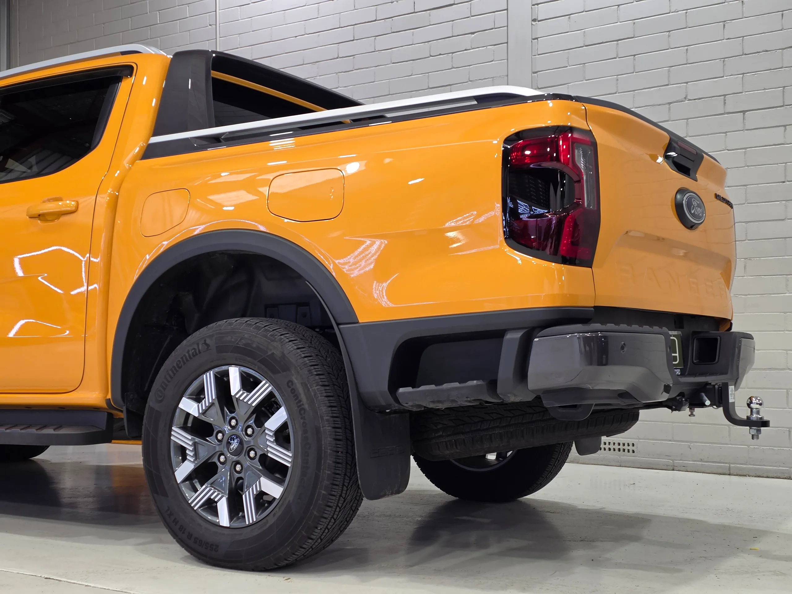 Low rear-quarter detail of an orange Ford Ranger Wildtrak PHEV, with the rear wheel and tow bar