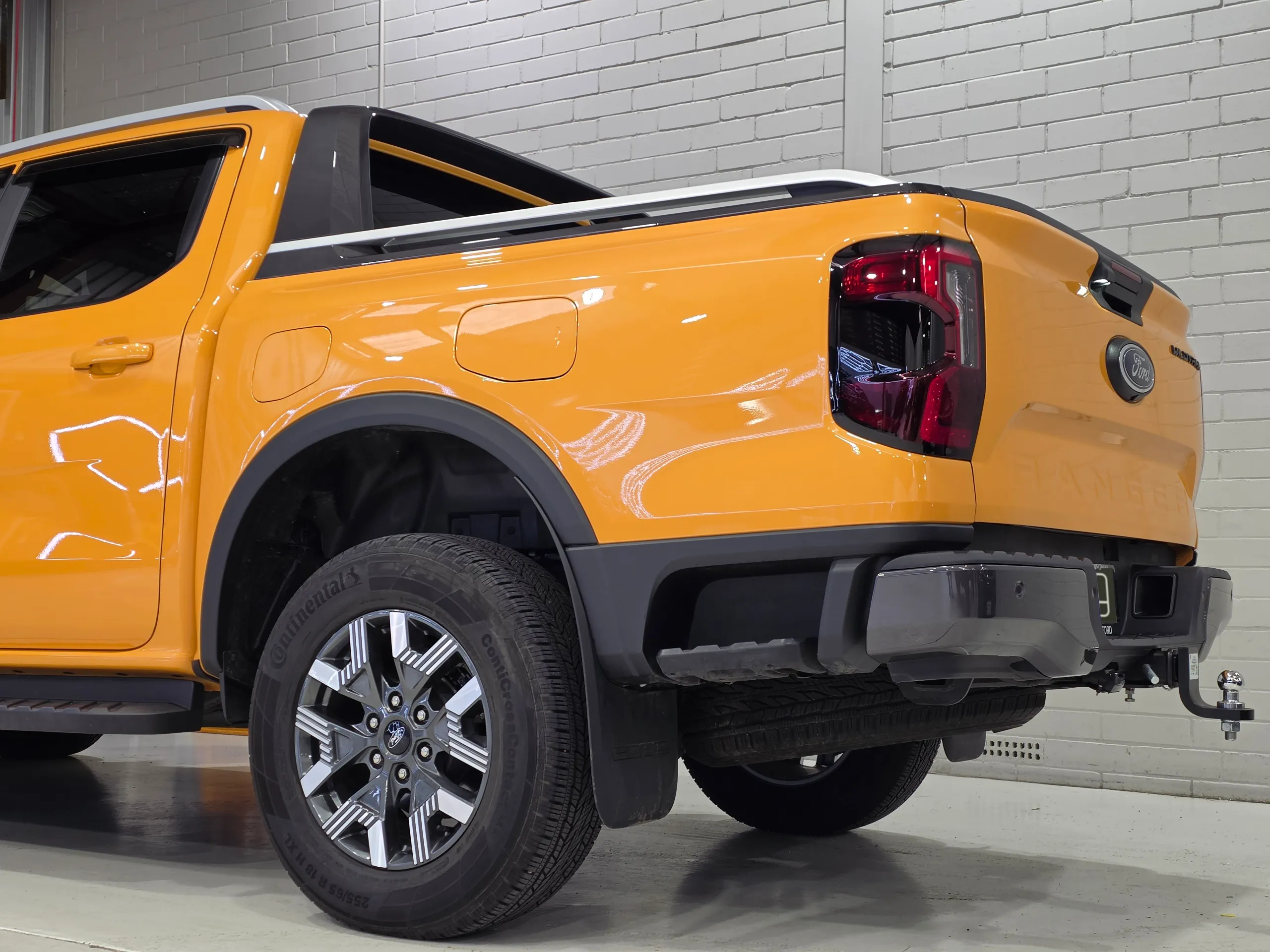 Orange Ford Ranger Wildtrak PHEV rear quarter and wheel against a white workshop wall